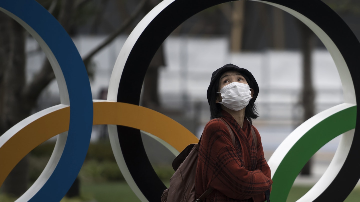 A woman wearing a face mask walks past the Olympic rings in front of the new National Stadium, the main stadium for the upcoming Tokyo 2020 Olympic and Paralympic Games, on February 26, 2020 in Tokyo, Japan. Concerns that the Tokyo Olympics may be postponed or cancelled are increasing as Japan confirms 862 cases of Coronavirus (COVID-19) and as some professional sporting contests are being called off or rescheduled