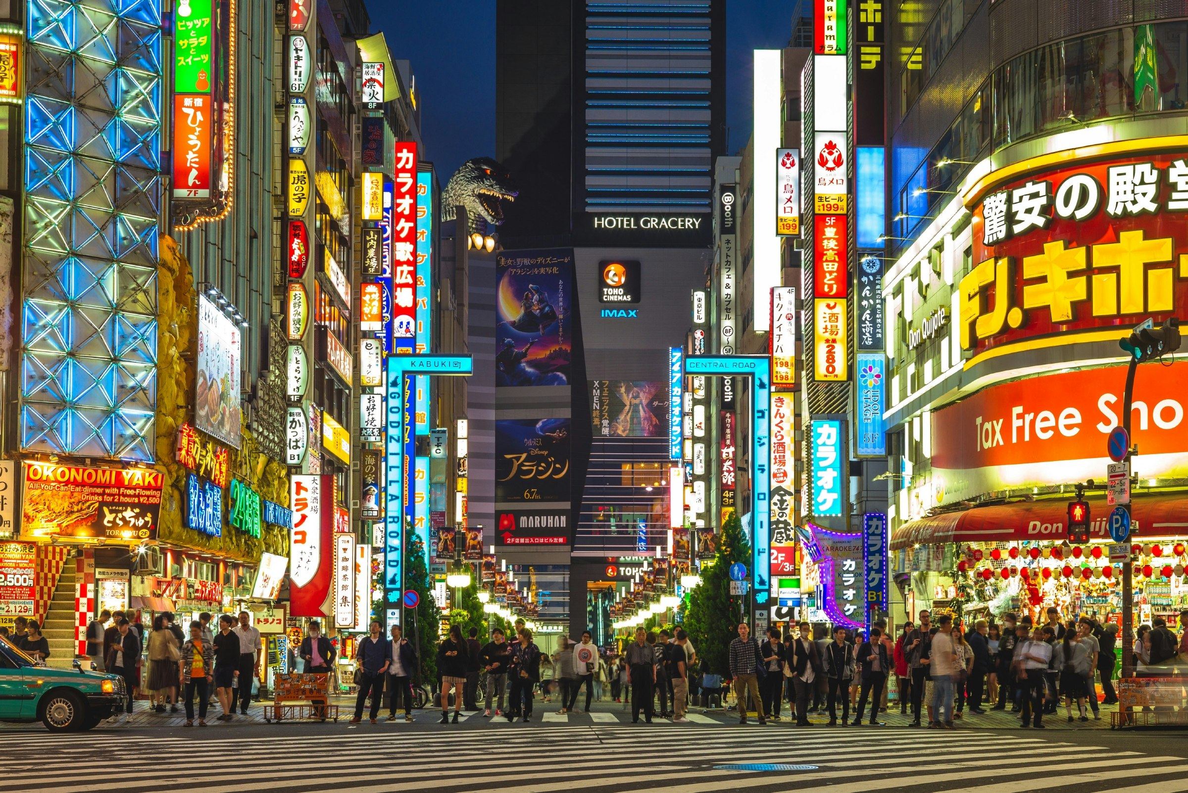 Shinjuku street in Tokyo at night. The neon lights from the shopfronts light up the street, which is full of people walking by.