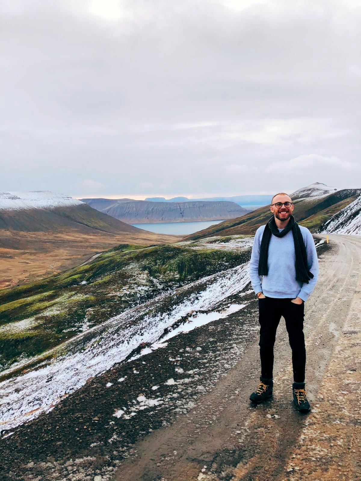 Writer Tom poses in front of mountainous, snowy Westfjords scenery in Iceland.