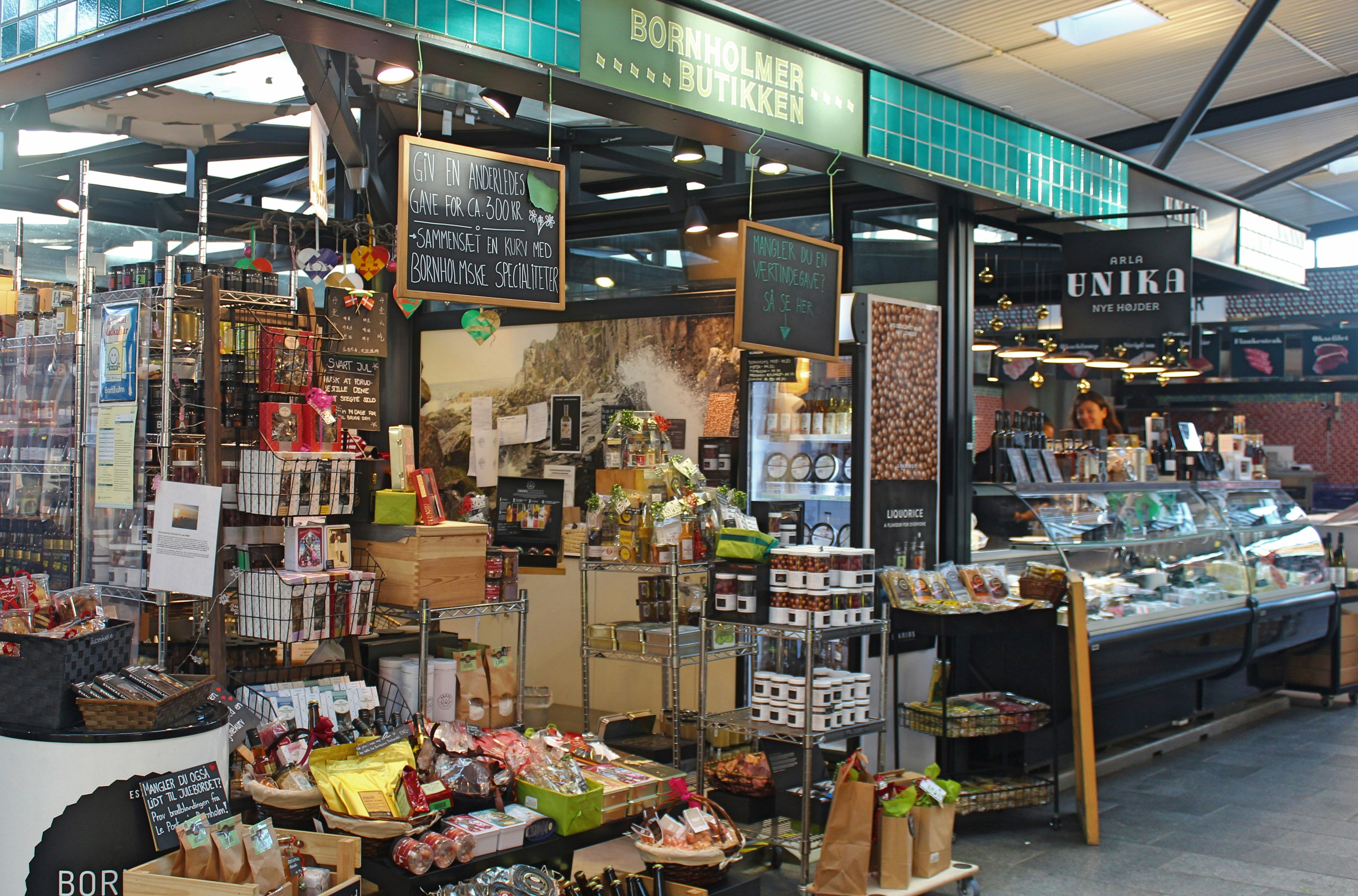 Stands at Copenhagen's Torvehallerne indoor food market; many products are displayed on racks and tables, and in glass display cabinets.