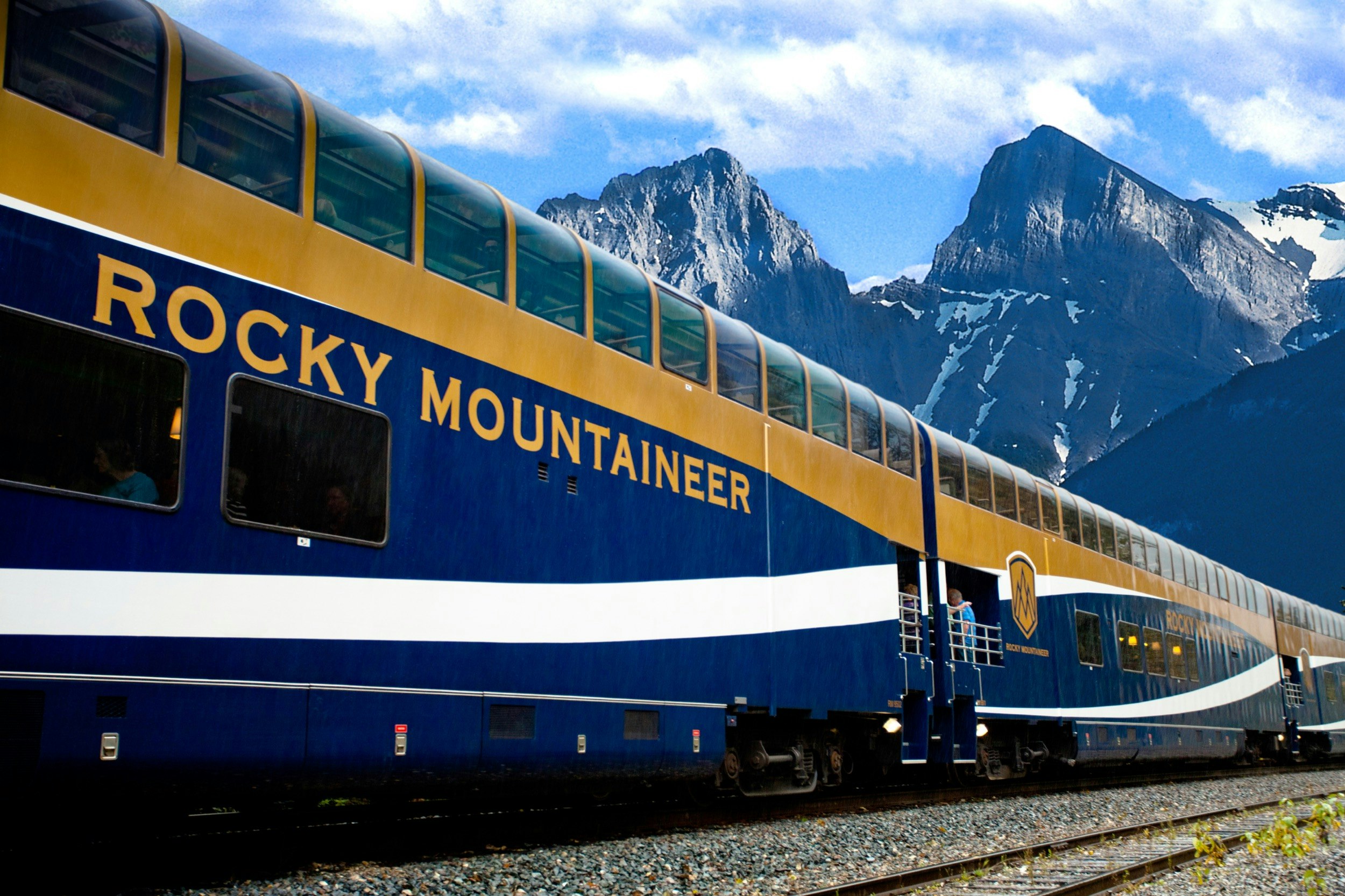 Looking up at a GoldLeaf service passenger car on the Rocky Mountaineer train with a craggy peak in the background