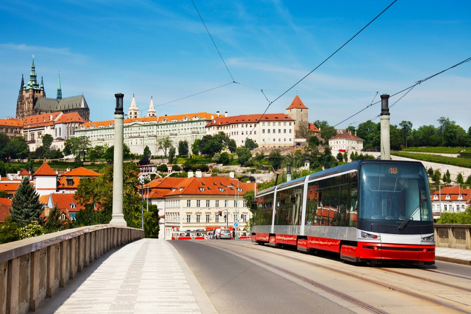 A red and white tram drives down a road with white buildings behind