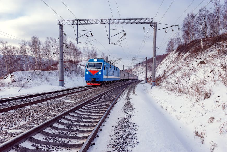 Snötäckta tågspår med ett blått-rött tåg som närmar sig