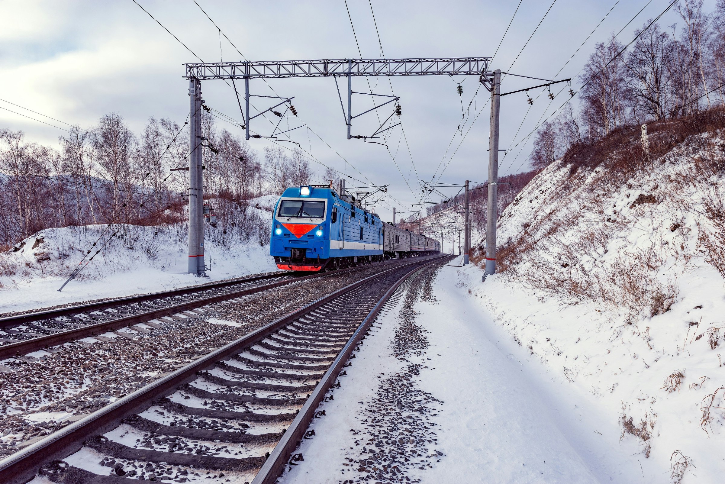 Snow-covered train tracks with a blue-and-red train approaching