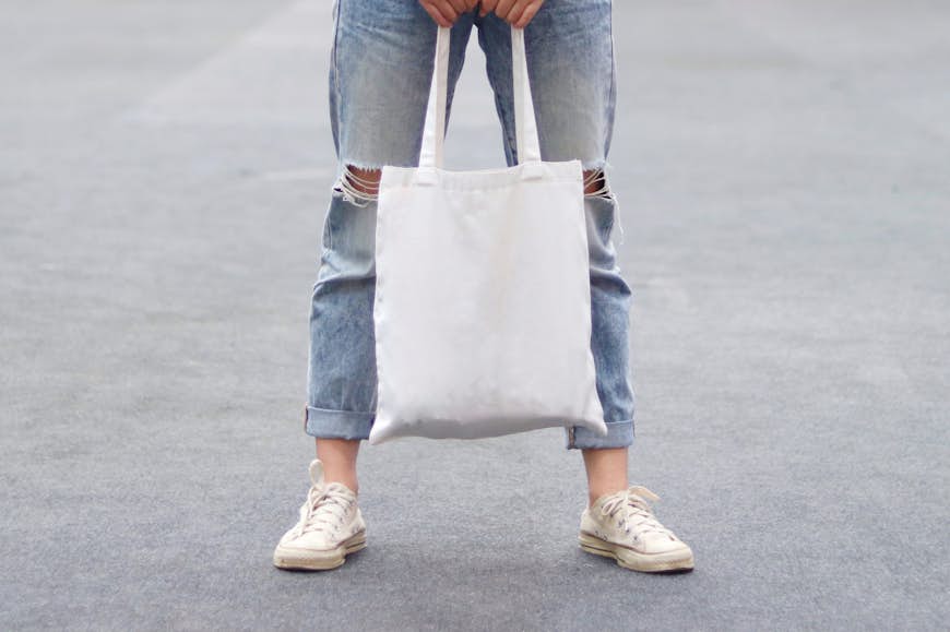 En kvinna som bär trasiga jeans håller i en vit väska.