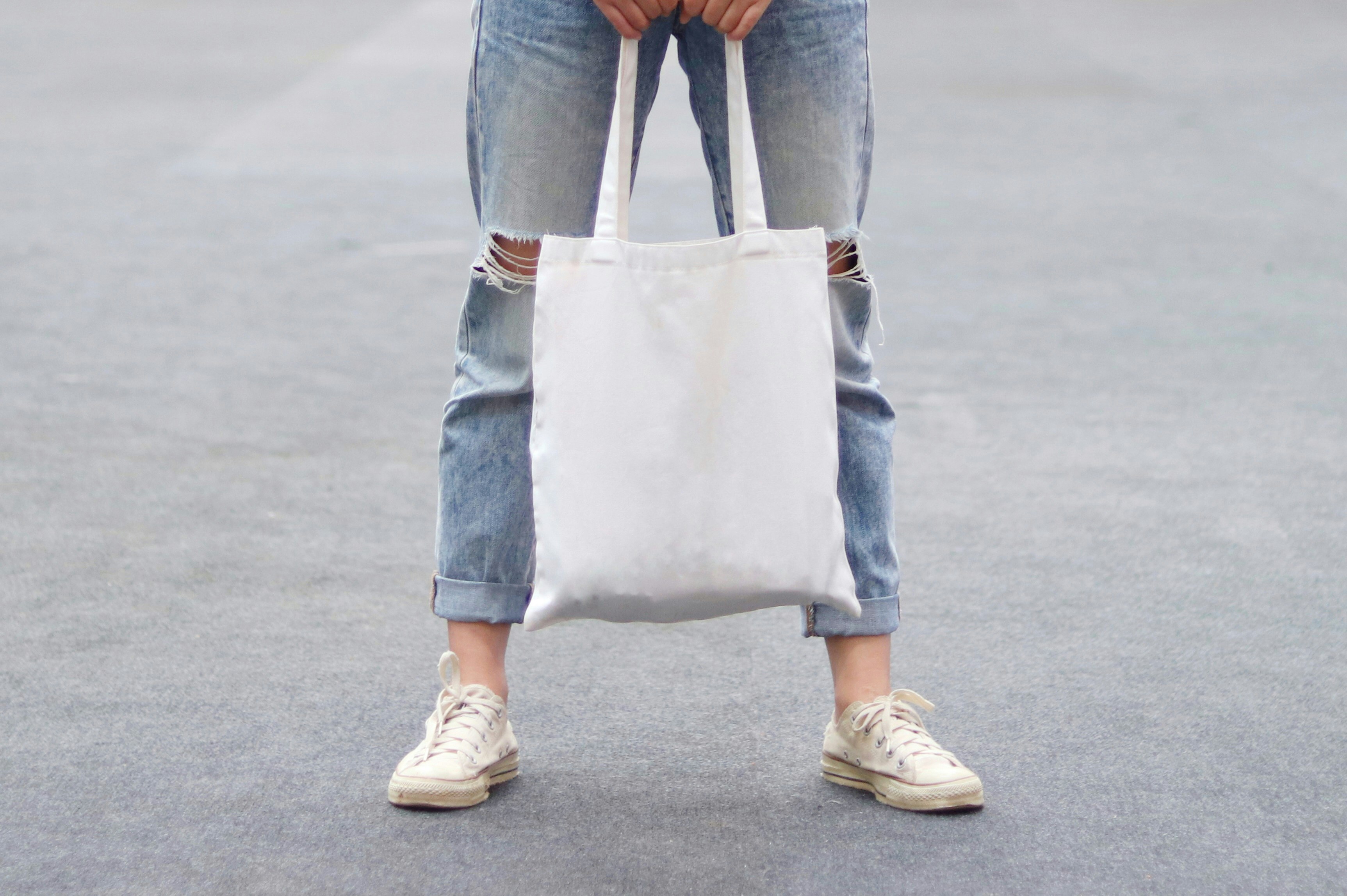 A woman wearing ripped jeans holds a white tote bag.