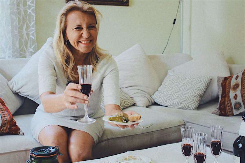 Woman drinking a glass of red wine offering a dish to someone off-camera.jpg