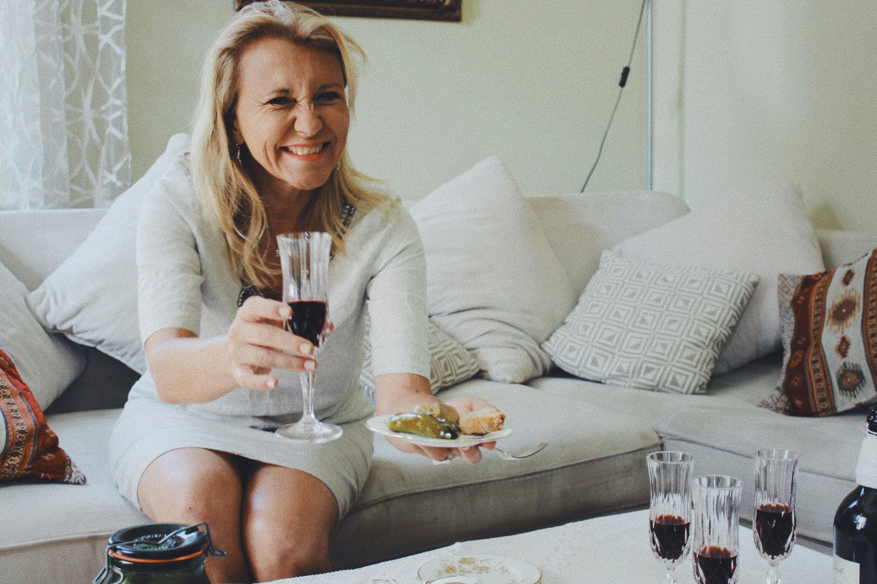 Woman drinking a glass of red wine offering a dish to someone off-camera.jpg