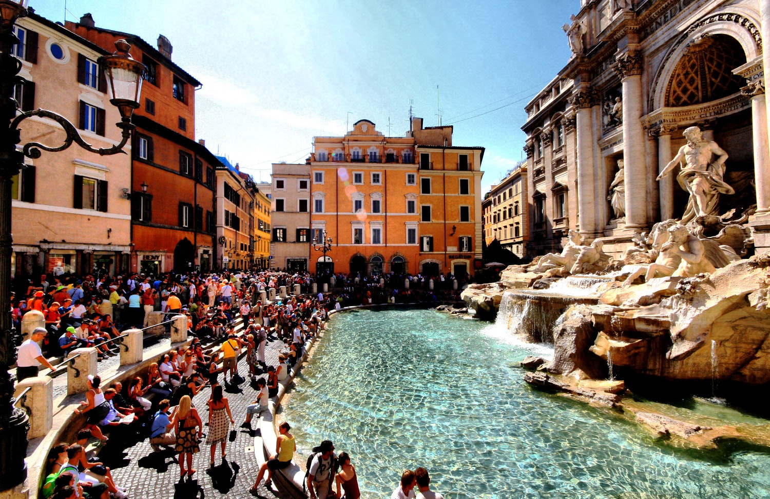 A large number of tourists take photos, throw coins and walk around Trevi Fountain in Rome.