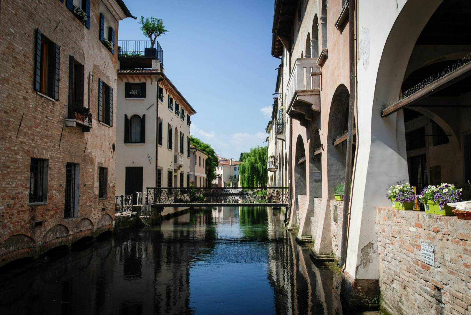 A bridge stretches between two buildings across a canal in Treviso