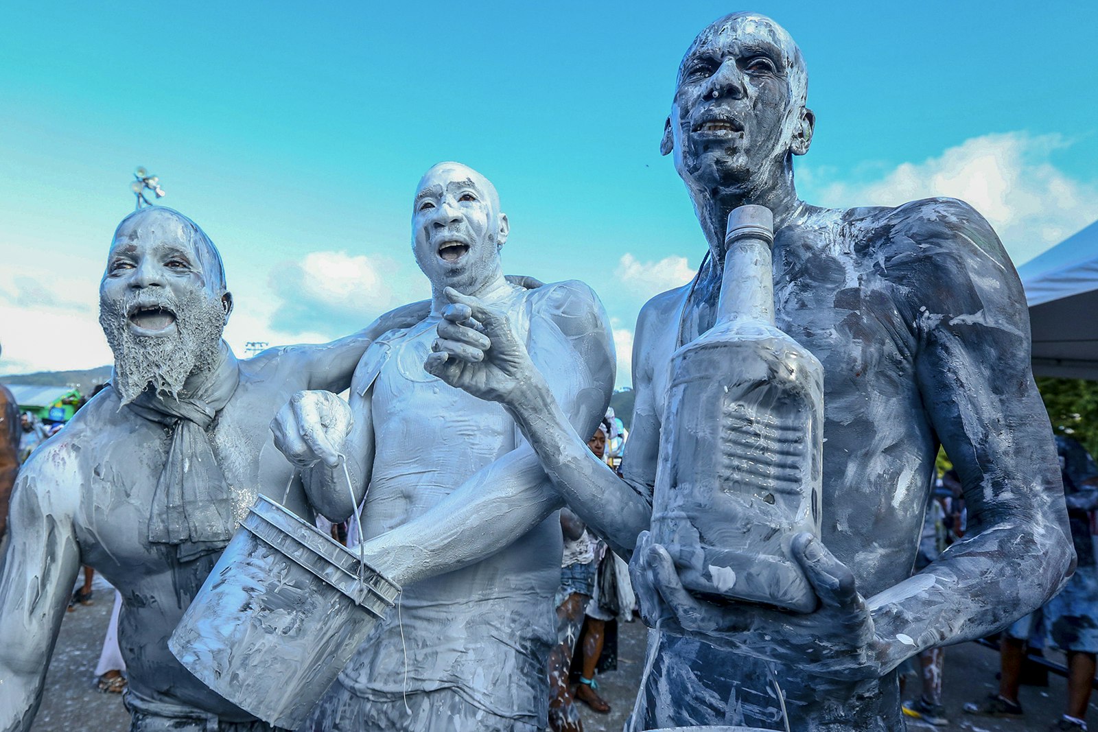 Three men covered in white paint hold a bucket and bottle while singing/cheering