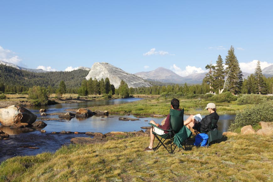 Two campers sit near a river in Yosemite National Park, California