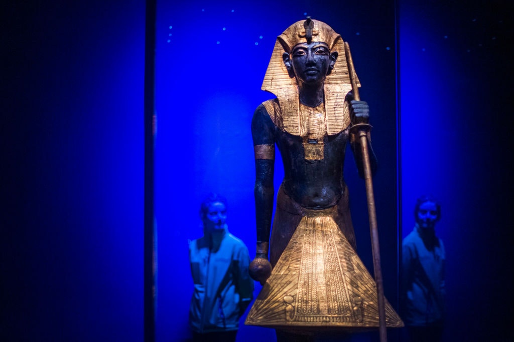 A museum staff member looks at a wooden guardian statue of King Tut