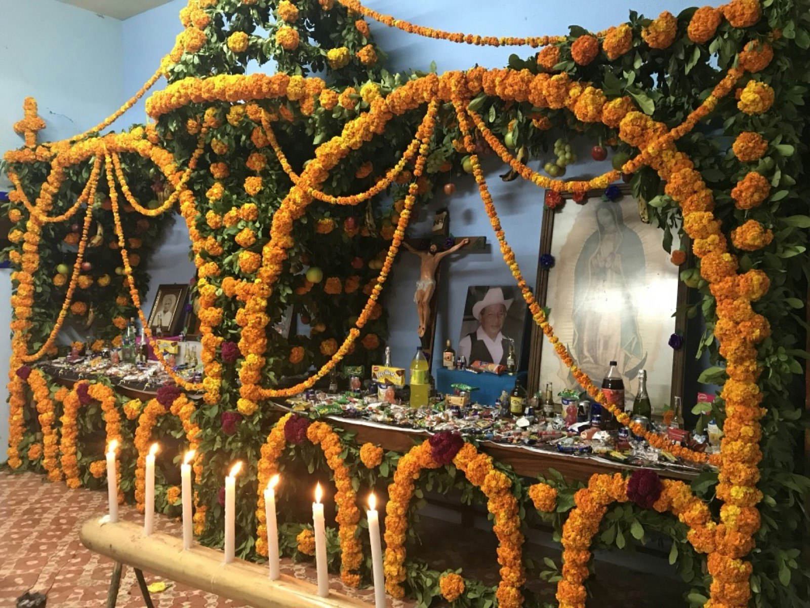 Strings of orange marigolds are draped over a wooden altar filled with photos and lighted candles; Xantolo