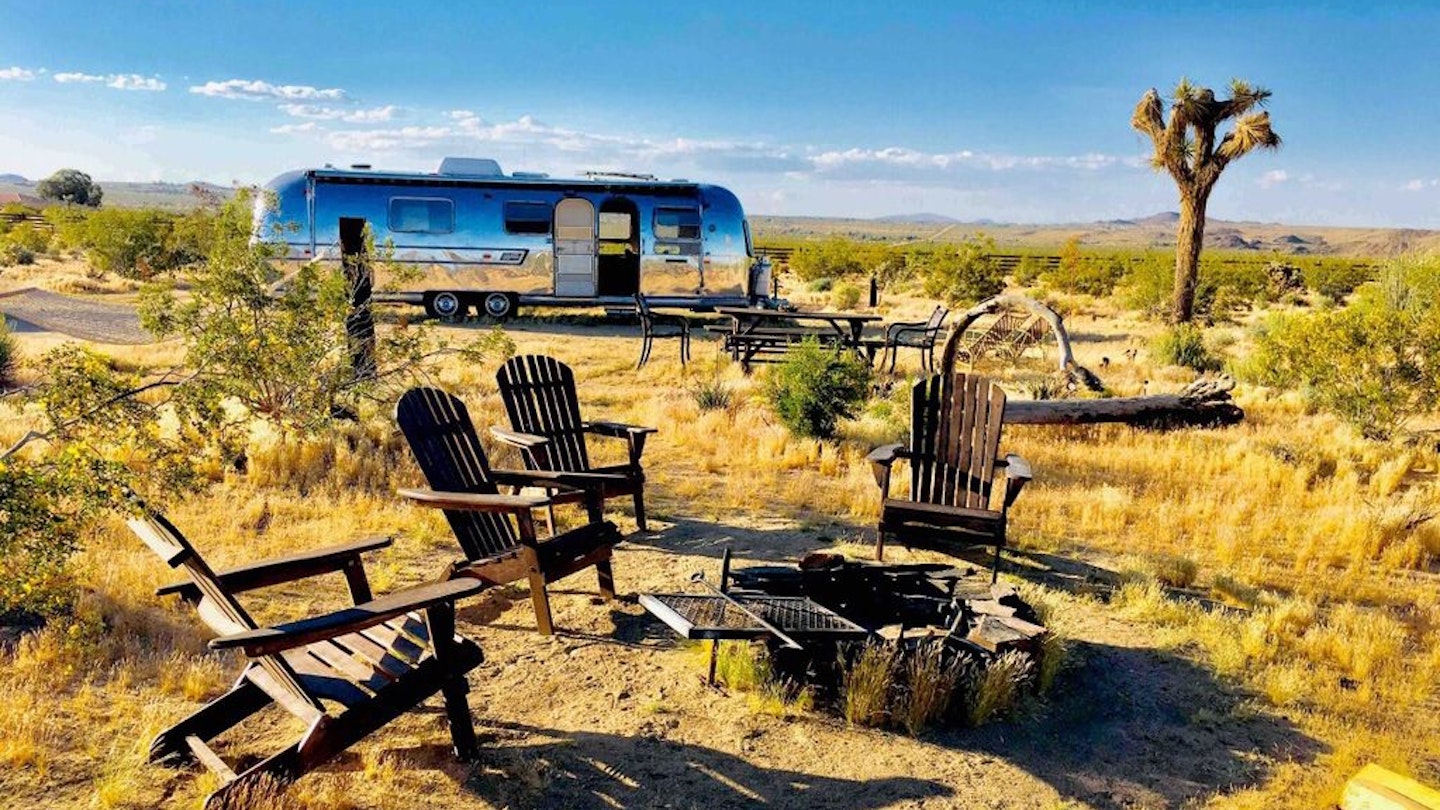 An Airstream trailer at Joshua Tree, with four Adirondack chairs around a fire pit