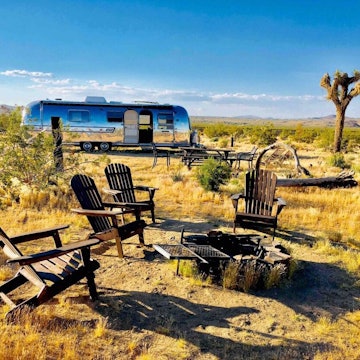 An Airstream trailer at Joshua Tree, with four Adirondack chairs around a fire pit