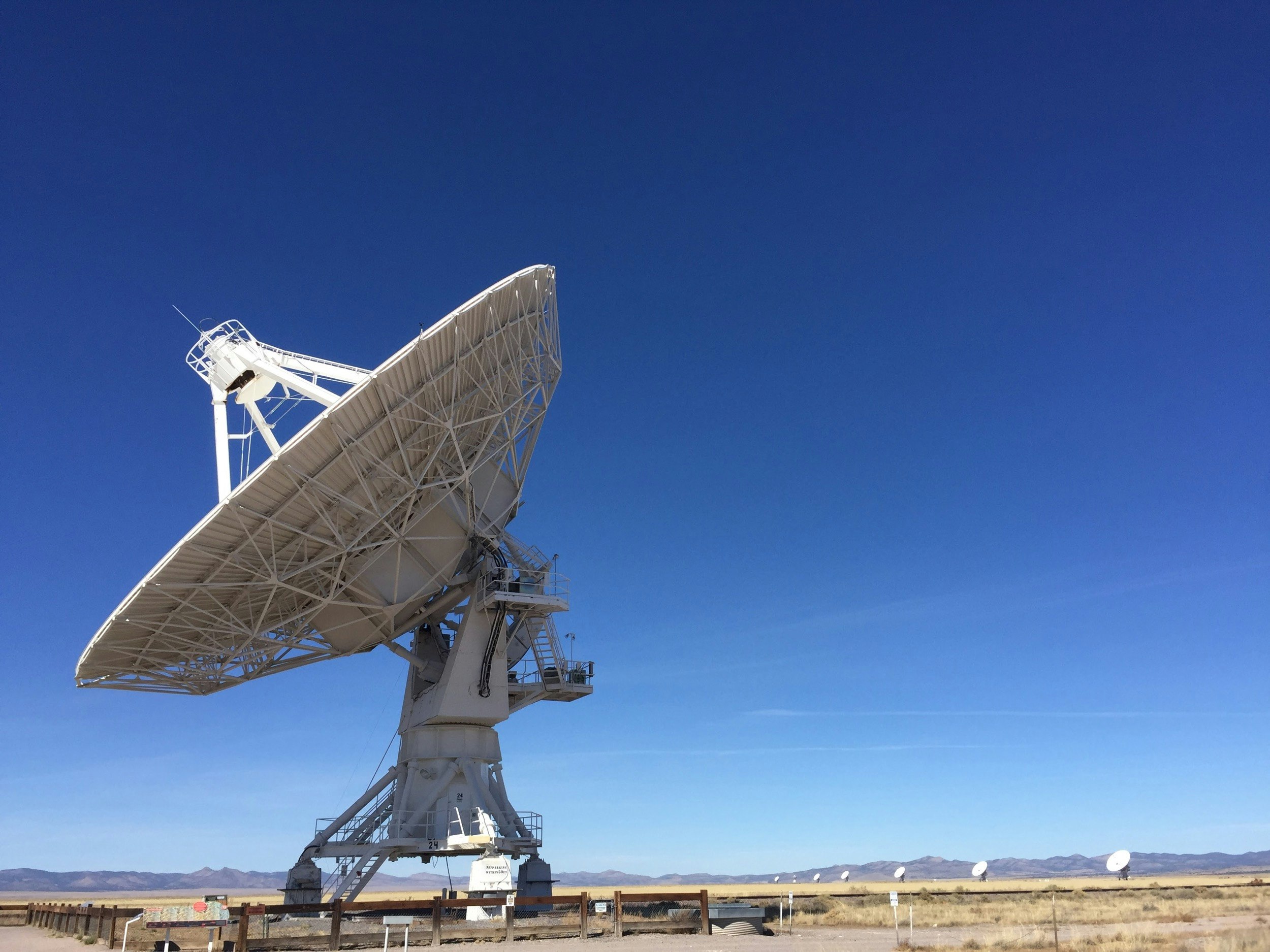 A large white radio dish stands out on a deep blue sky