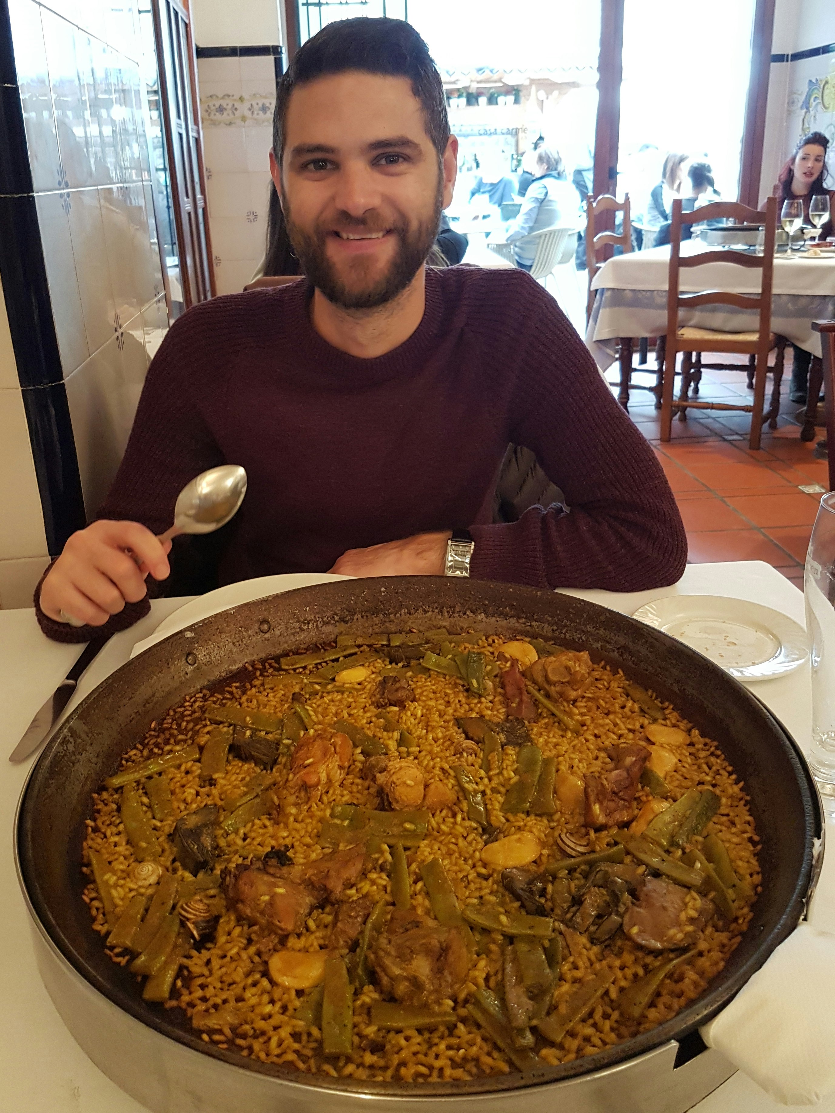 Writer Robert Kidd is sitting in a restaurant, with a huge pan containing traditional paella in front of him. Spoon in hand, waiting to dish up, he smiles broadly at the camera.