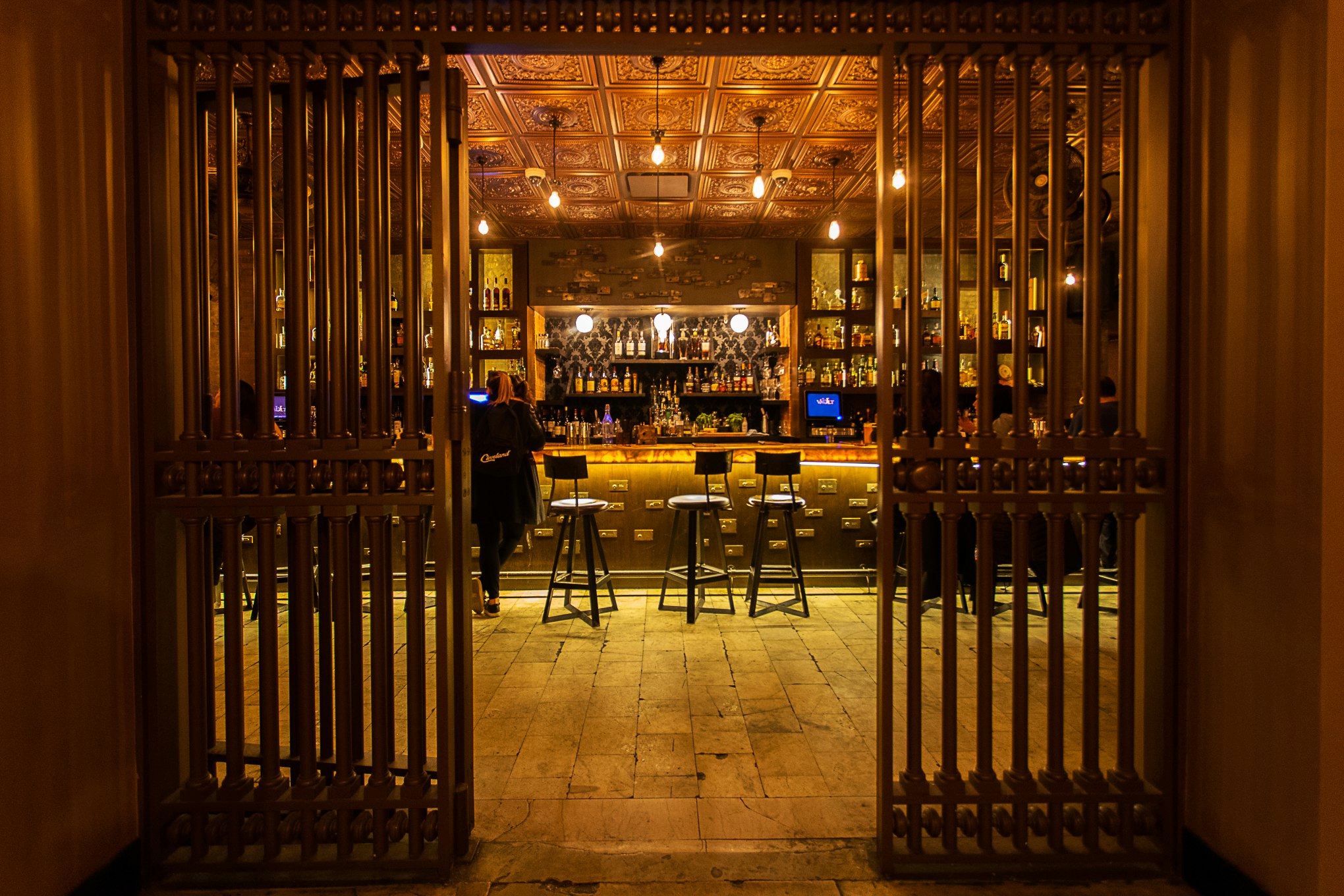 A large, gold-colored metal grate has been pulled back to reveal the elegant bar at Vault, in Metropolitan at The 9.