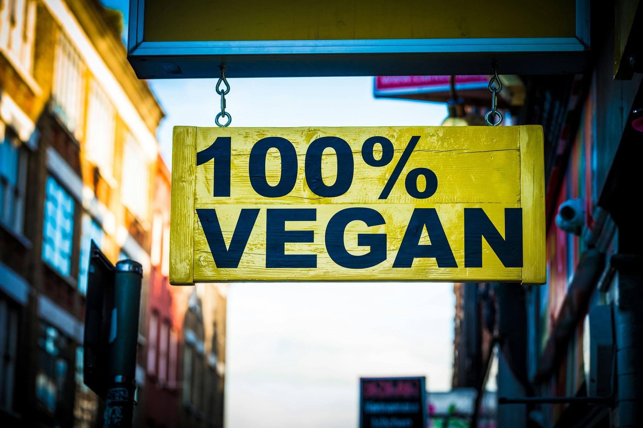 Close up color image depicting a yellow sign on a city street in London, UK, saying in bold black lettering, 100% vegan. 