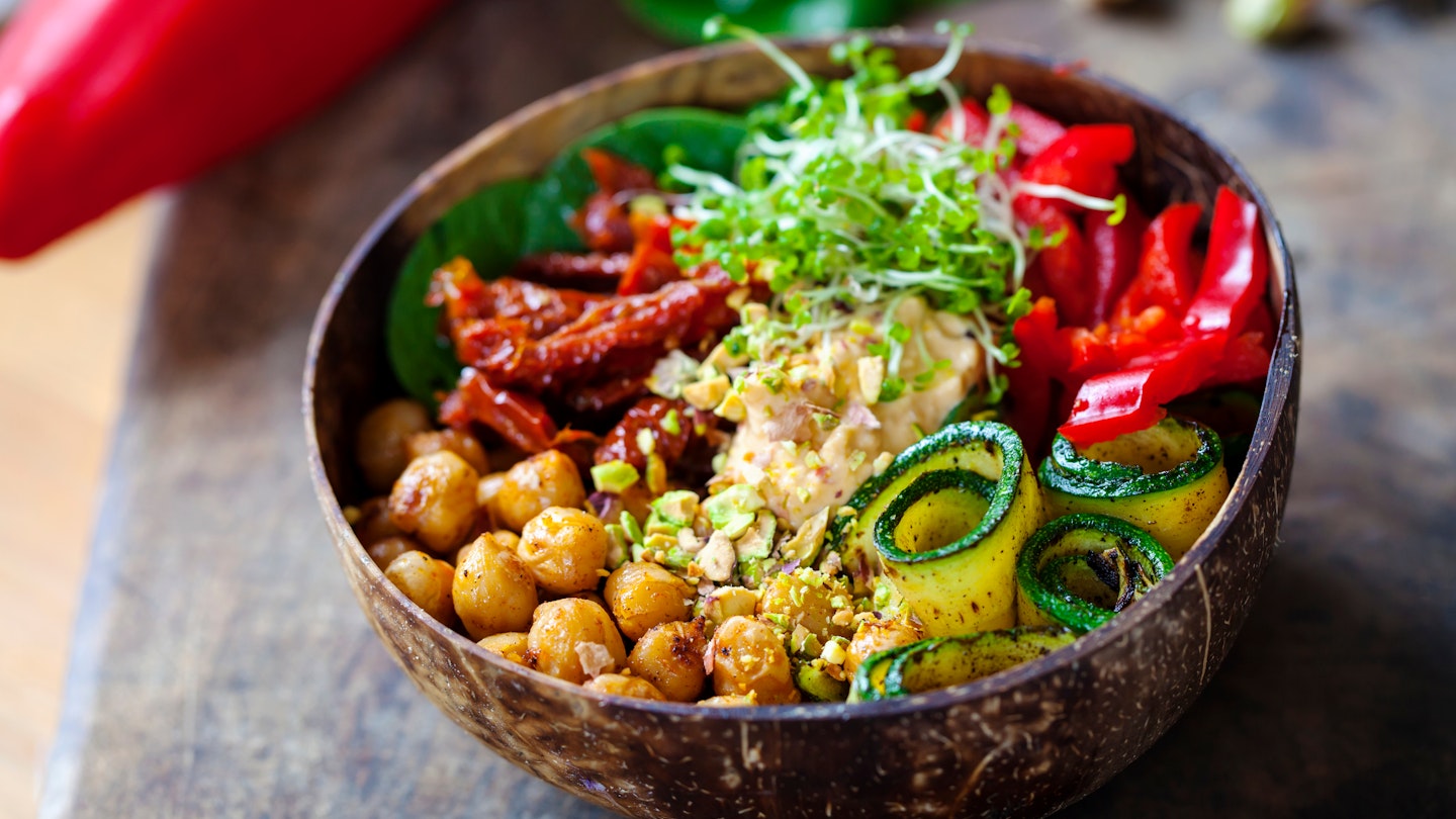 Closeup of a bowl filled with chickpeas, cucumbers, red peppers, sun-dried tomatoes and grains