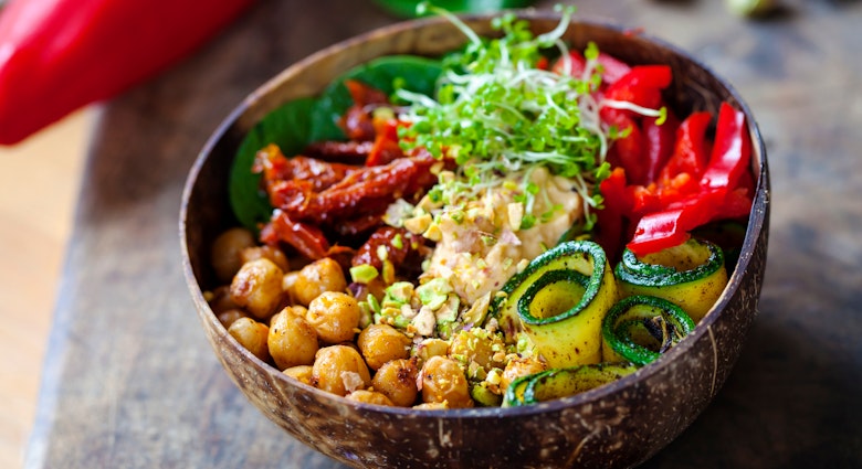 Closeup of a bowl filled with chickpeas, cucumbers, red peppers, sun-dried tomatoes and grains
