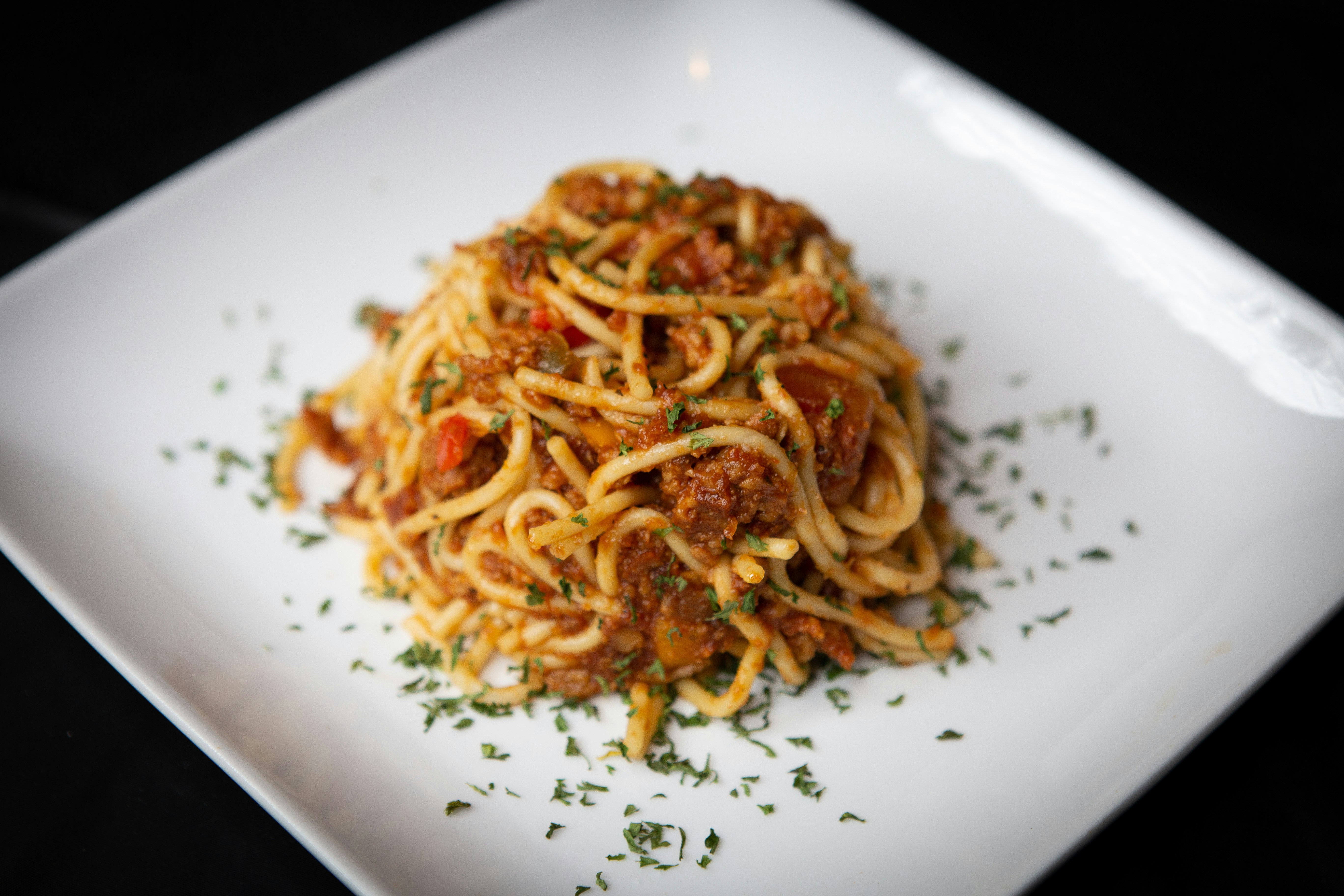 A closeup of vegan spaghetti and meat sauce sprinkled with green herbs on a white plate