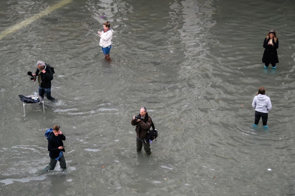 People walk across and take photos at the flooded St. Mark's Square 