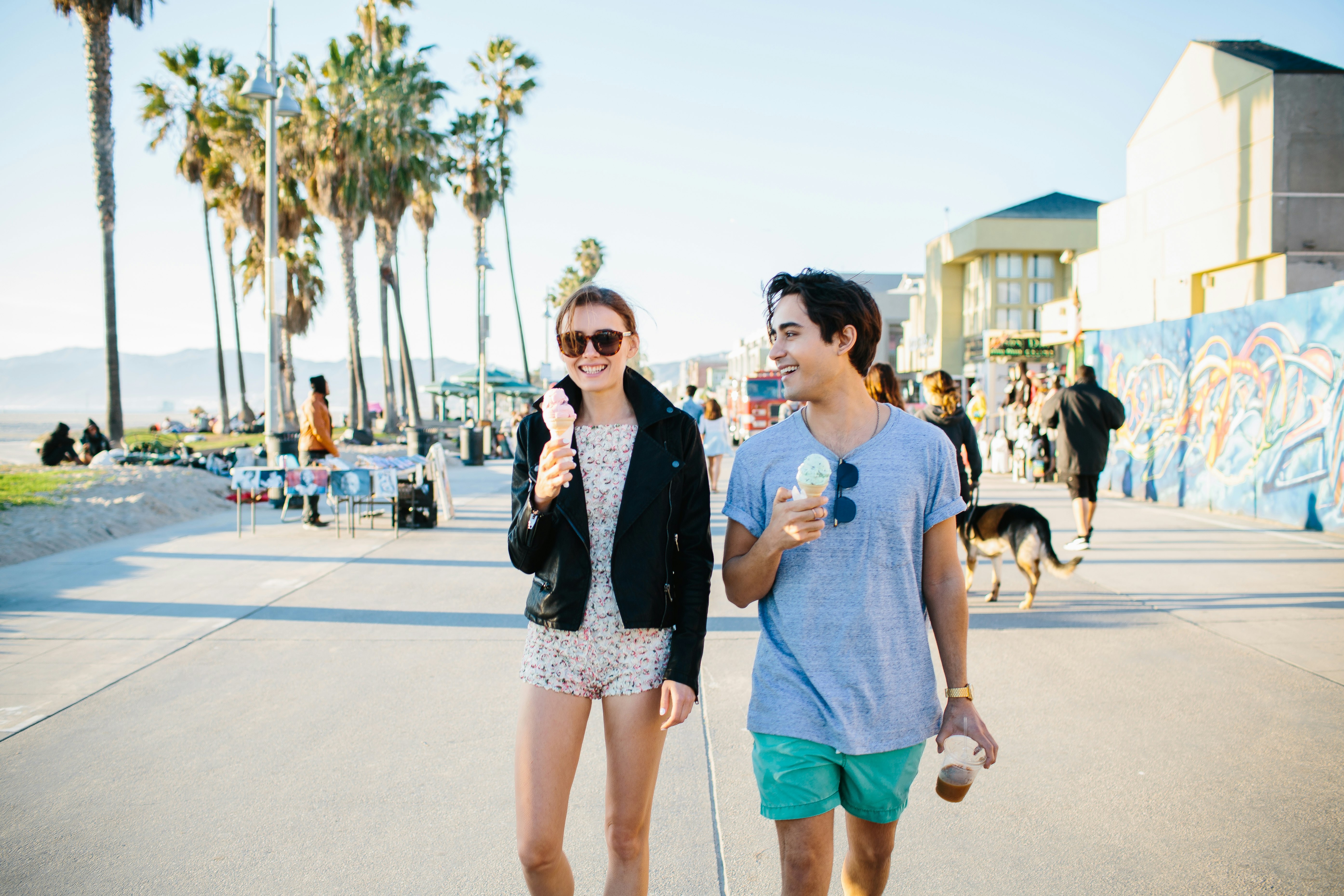 A young man and woman eat ice cream cones as they walk along the boardwalk in Venice Beach; California ice cream