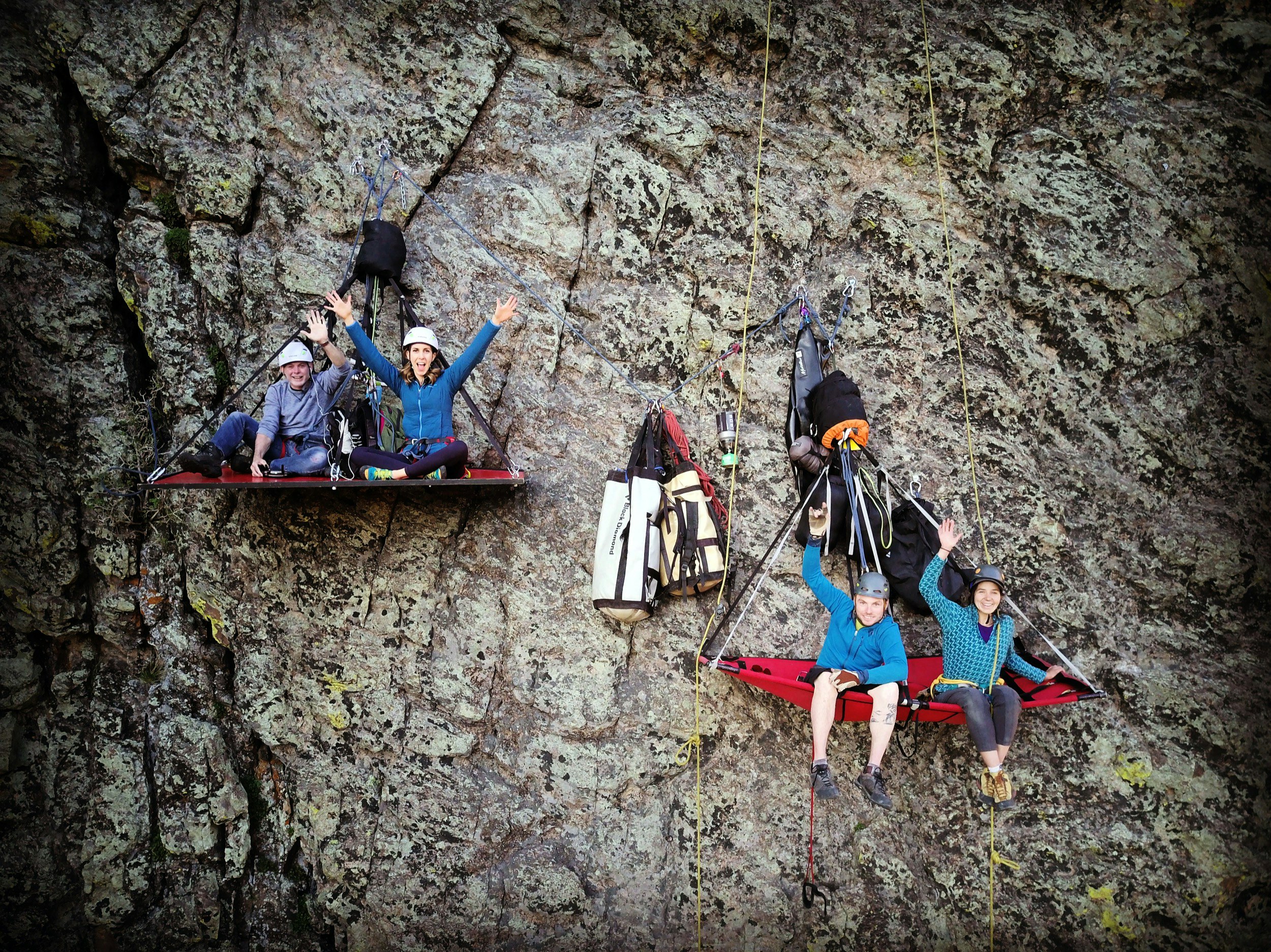 Four people sit on two small platforms attached to a cliff face they reached by via ferrata in Colorado