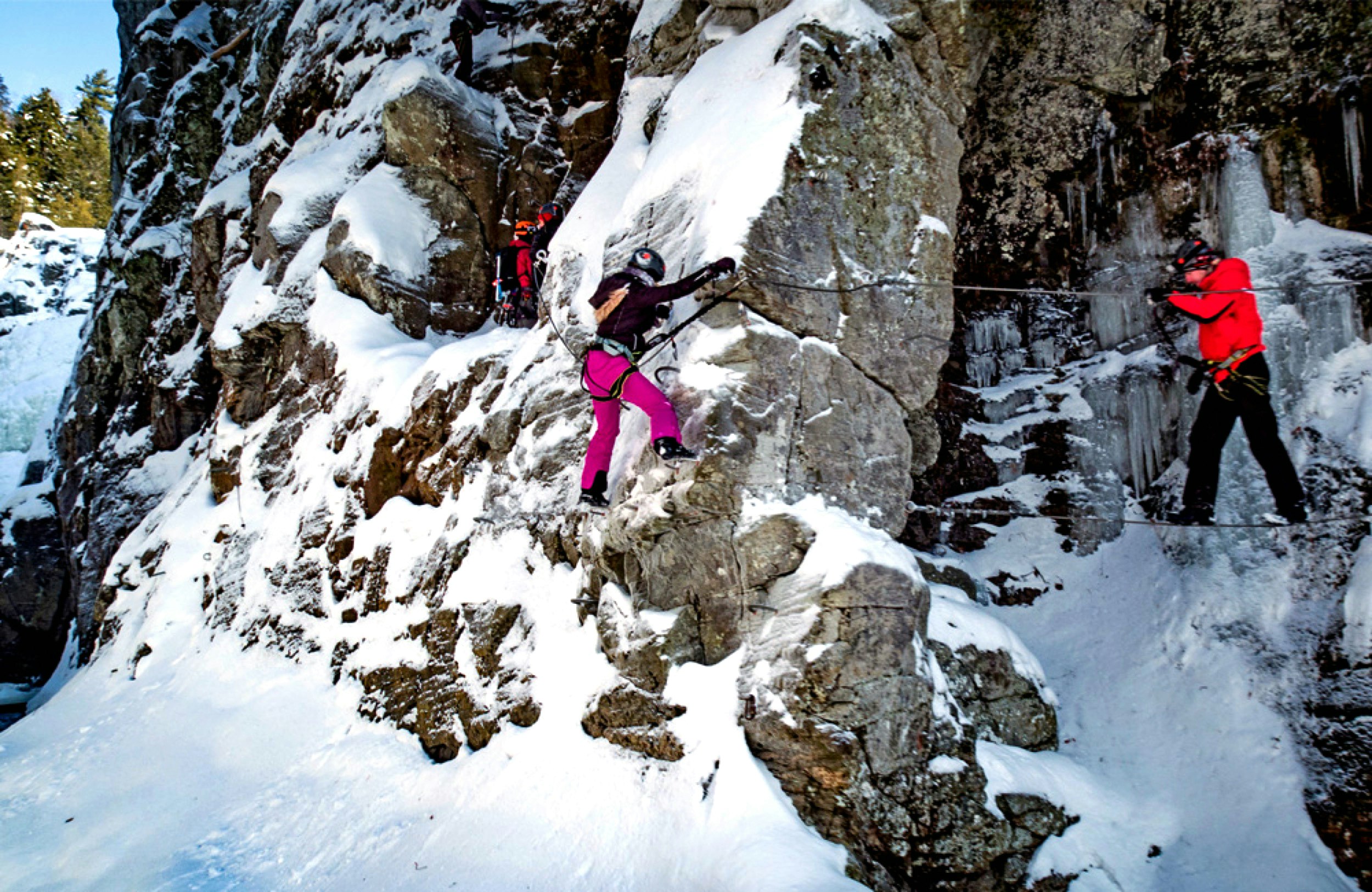 People use a via ferrata to cross a snowy cliff face