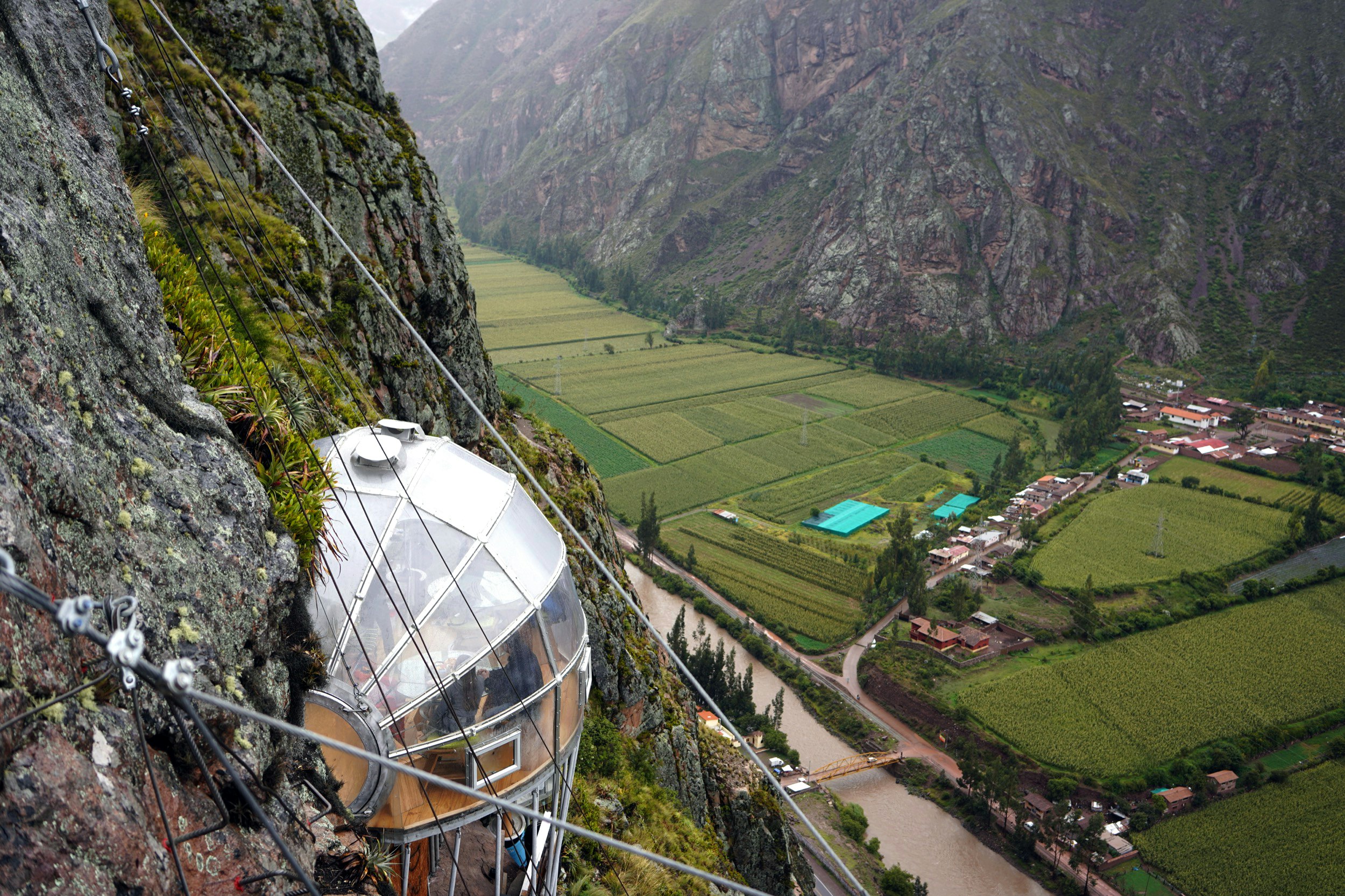 An impressive multi-level glass-walled pod is attached to a cliff face and accessible by via ferrata in Peru