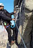 A man looks across a mountain range in Alaska as he hangs from a via ferrata