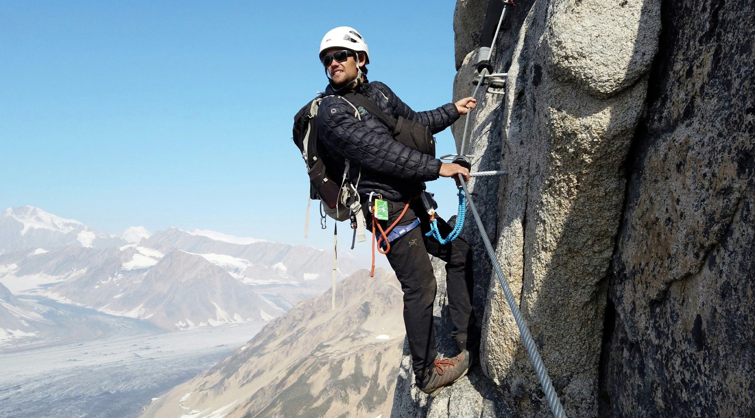 A man looks across a mountain range in Alaska as he hangs from a via ferrata
