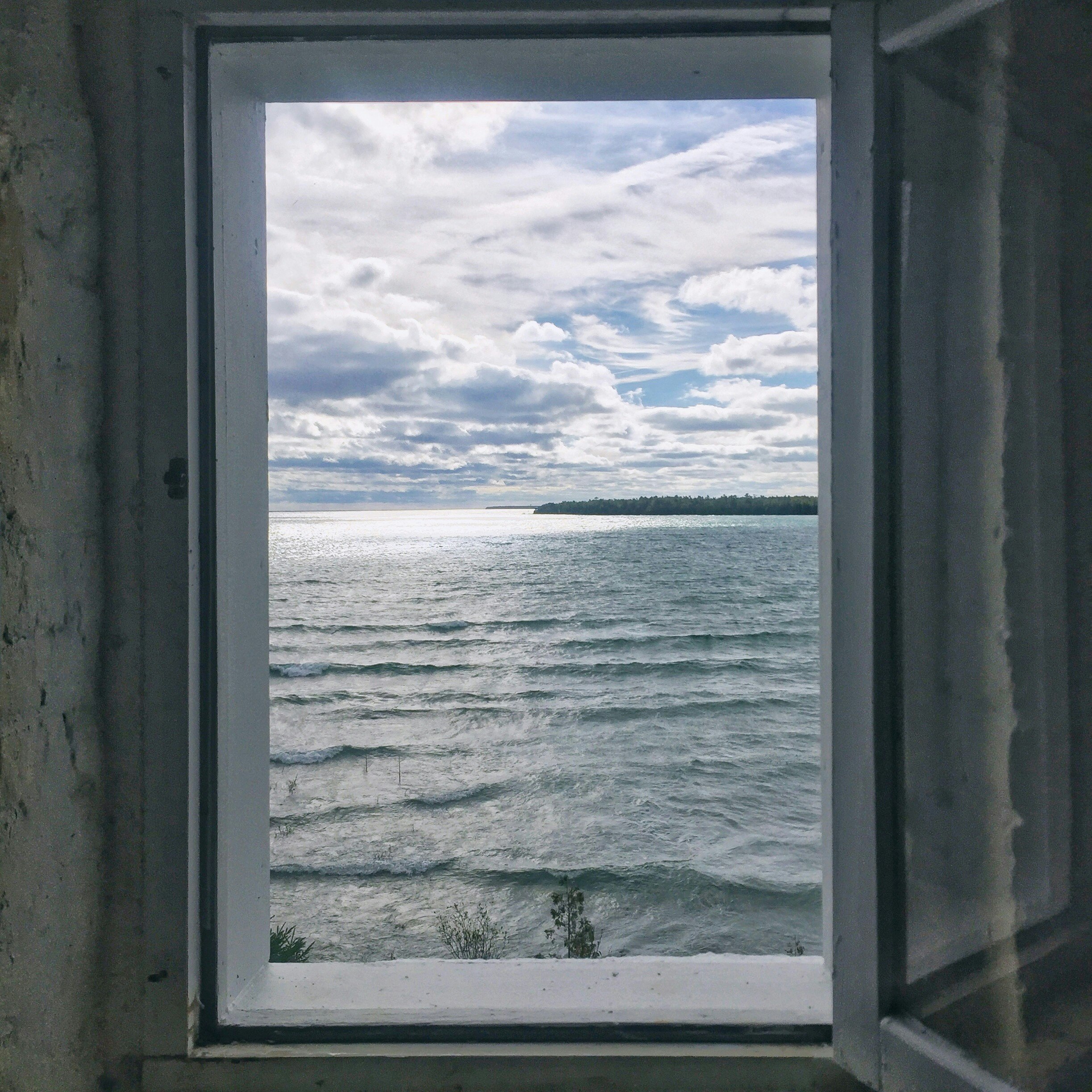 View of Lake Huron waves from Presque Isle Lighthouse in Alpena, Michigan. The scene is framed through a whitewashed window frame.