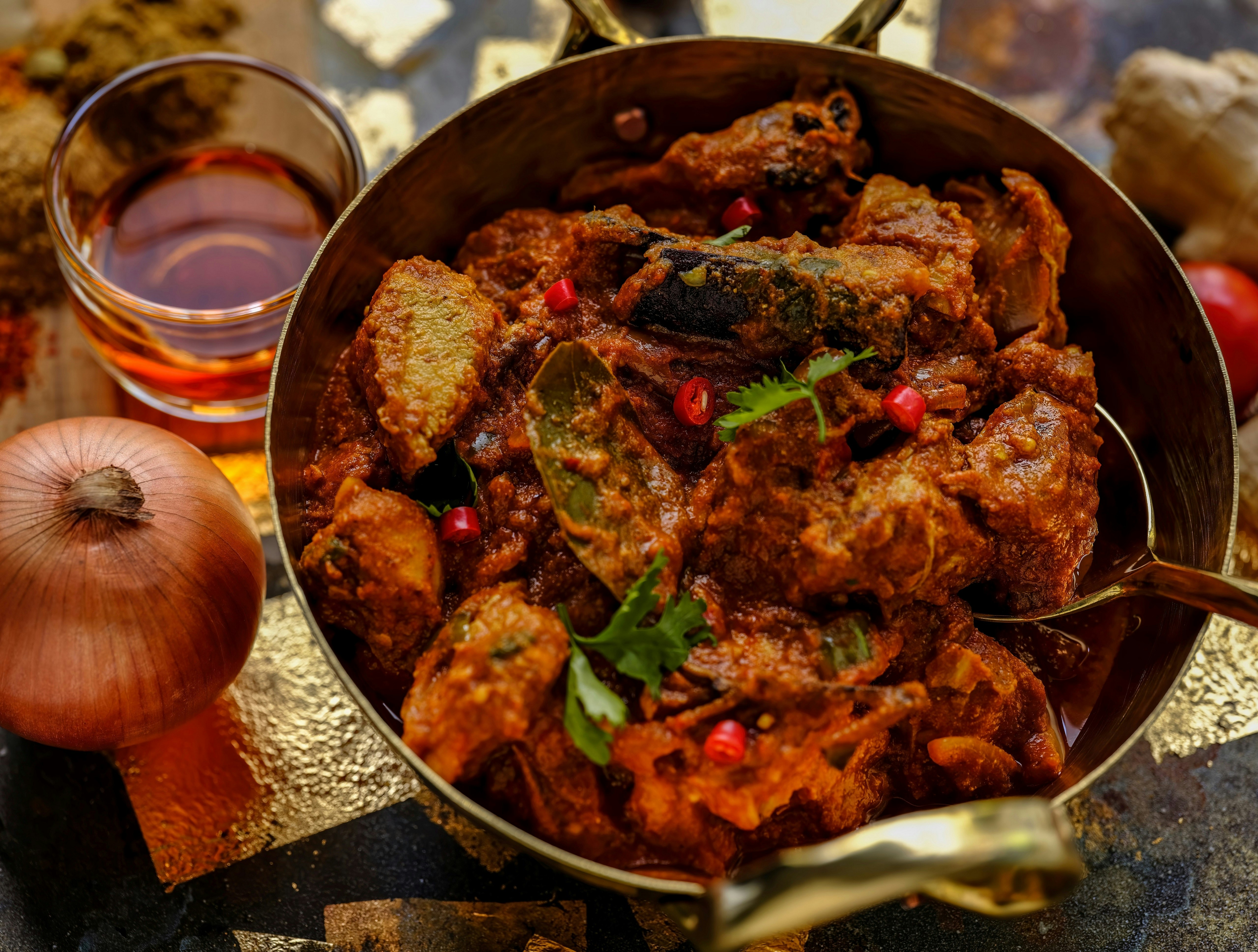 A top-down view of a vindaloo curry in a large circular pan. The curry consists of chicken and spices, and a thick brown sauce.