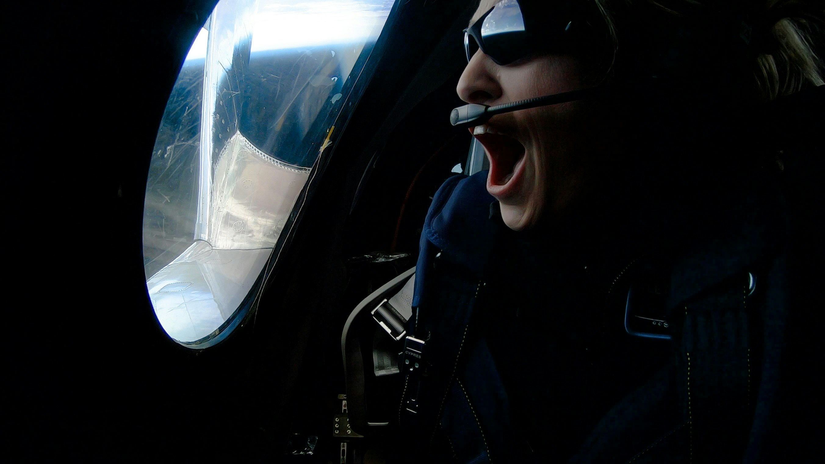 Virgin astronaut in space, wearing sunglasses and smiling while talking into a headset