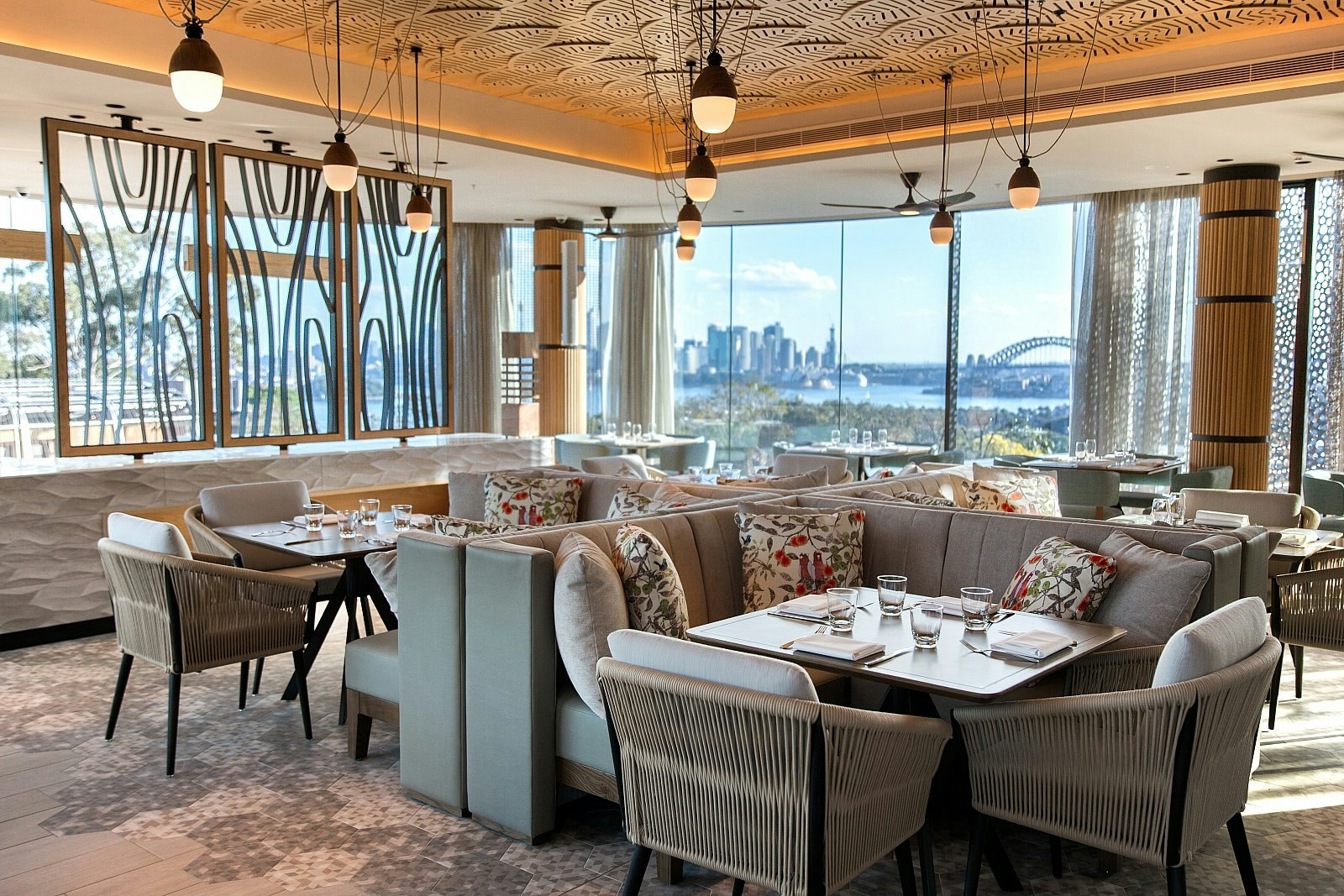 The Me-Gal restaurant interior, with modern furnishings, floral cushions on chairs, and panoramic views over Sydney Harbour.