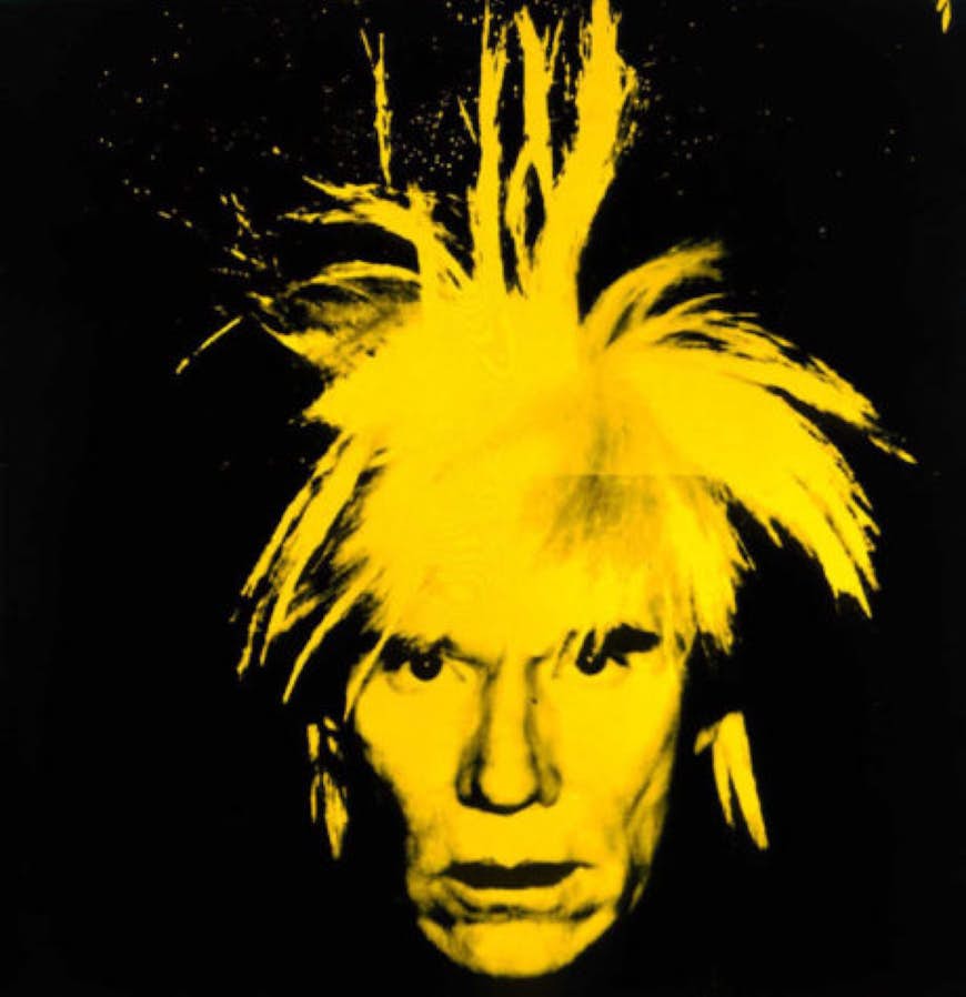 A yellow-hued Andy Warhol's hair stands on end, on a stark black background; Warhol in the US