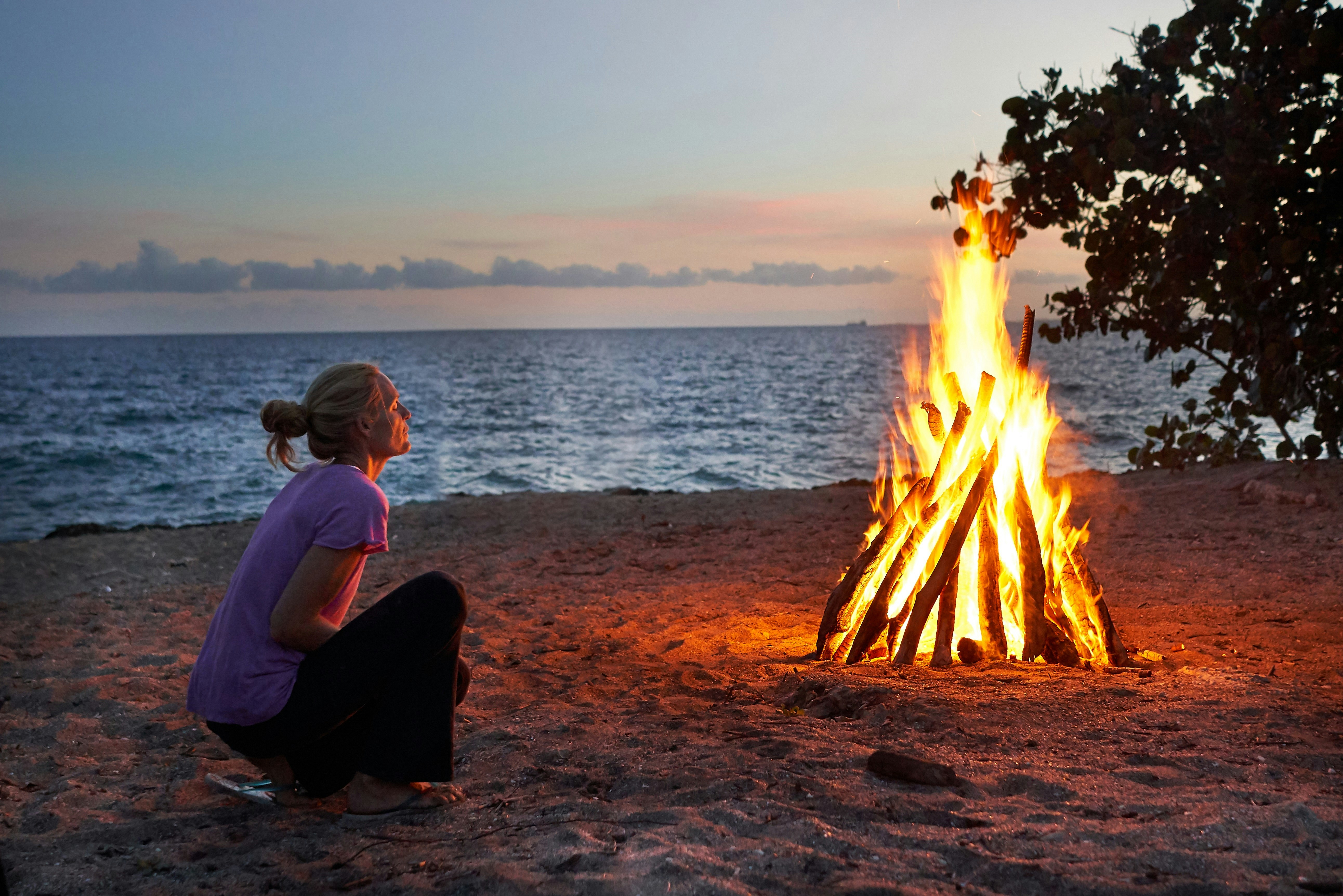 A woman sits by a campfire on the beach in the Dominican Republic at dusk