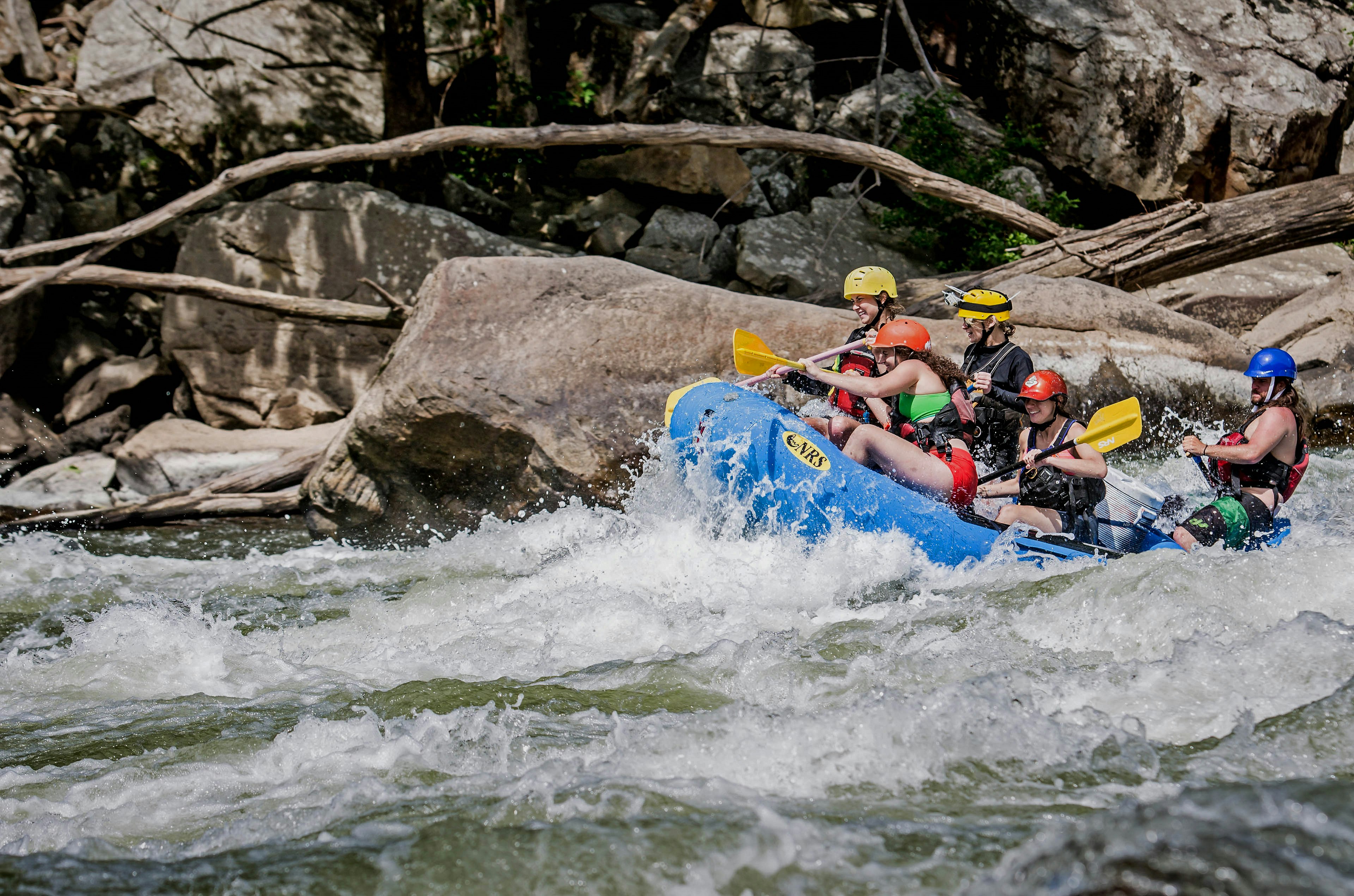 Large rocks are visible as a raft crashes through the rapids in West Virginia. A number of branches are also visible.
