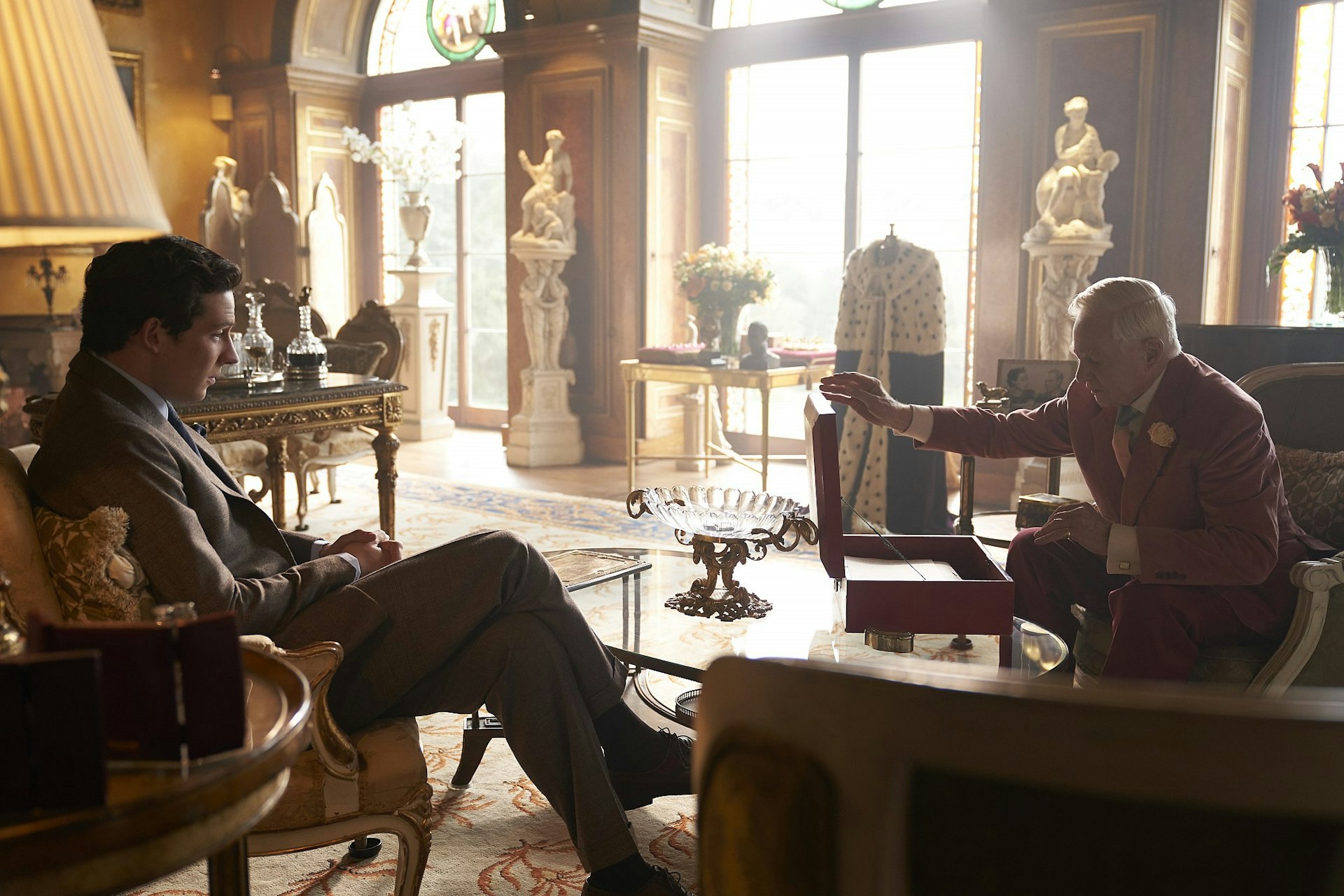 A still from The Crown season 3; it shows West Wycombe House doubling as the Duke of Windsor’s home, with the ailing duke and Prince Charles sat in an elegant drawing room.