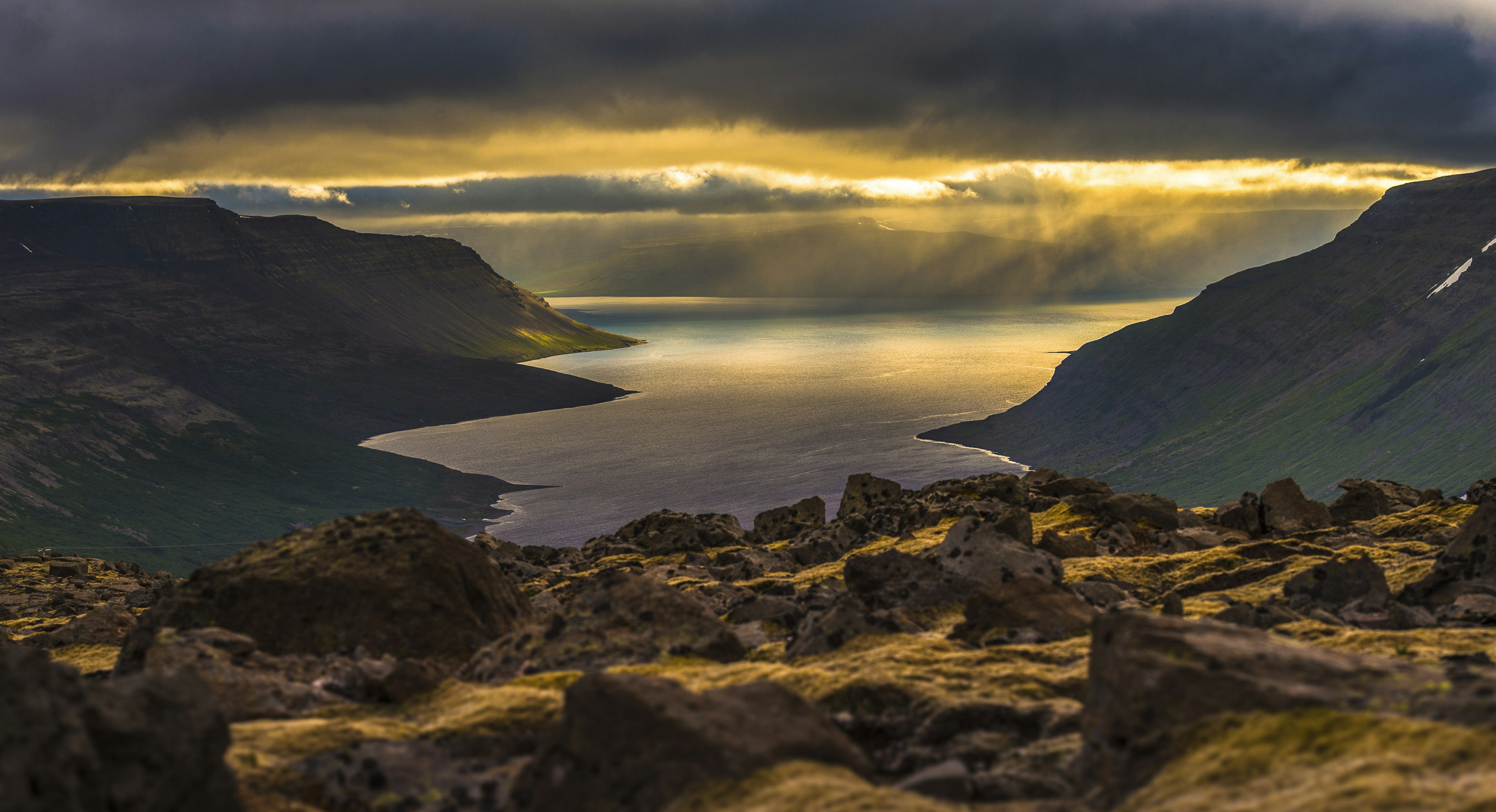 Looking over rocks towards fjord scenery in the Westfjords, Iceland, with sunset over the sea beyond.