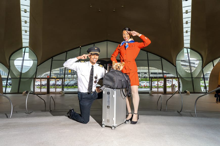 En pilot och en flygvärdinna står vid resväskan toppad med en liten hund i en Wild One Air Travel Carrier