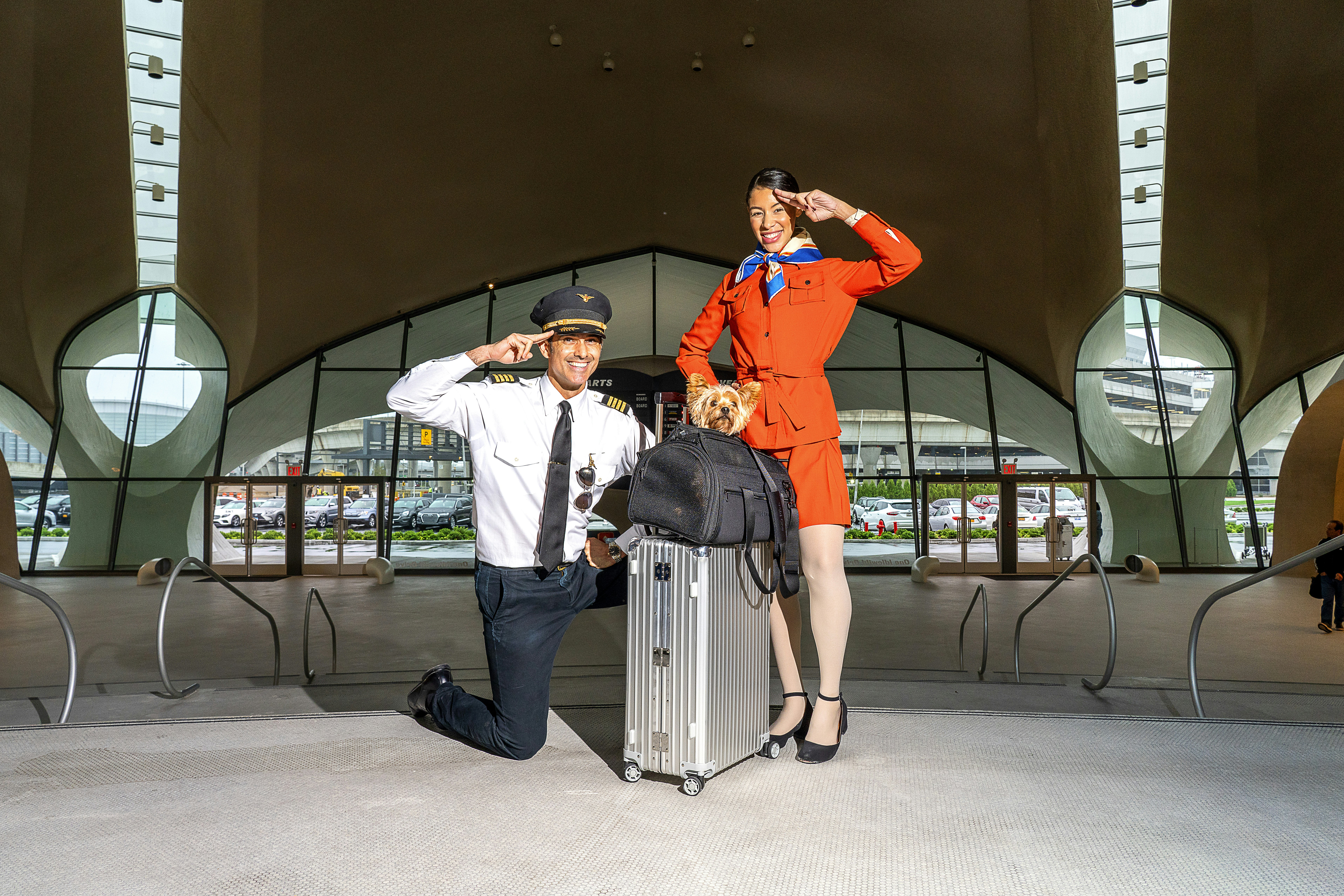 A pilot and a flight attendant standing by suitcase topped with a small dog in a Wild One Air Travel Carrier
