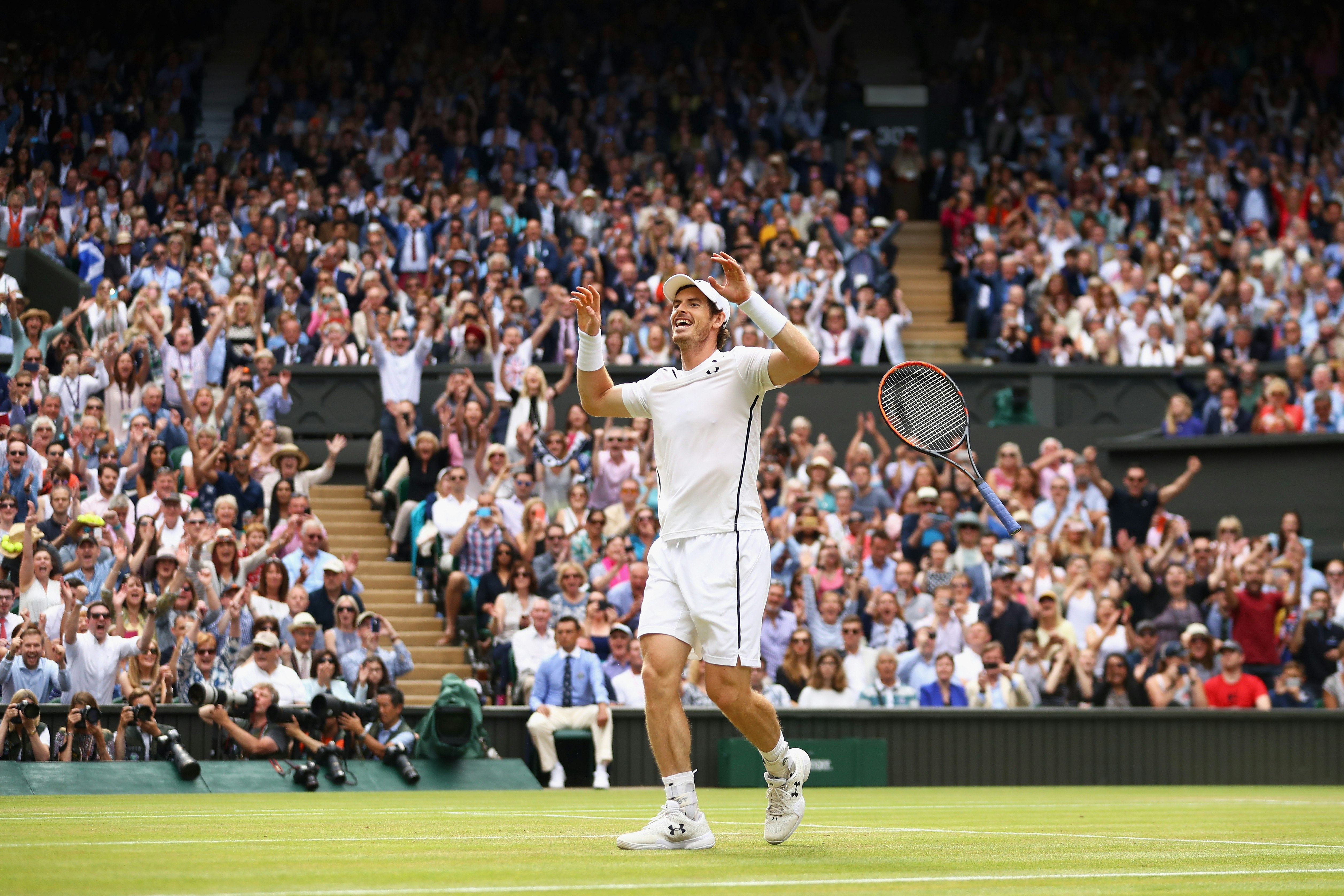 Tennis player Andy Murray celebrates at Centre Court during a Wimbledon Final. Rows of fans cheer in the background. 
