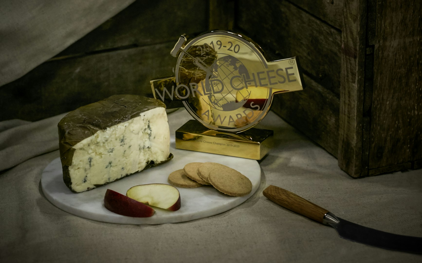 A blue cheese wheel, cut in half, is pictured beside a World Cheese Award