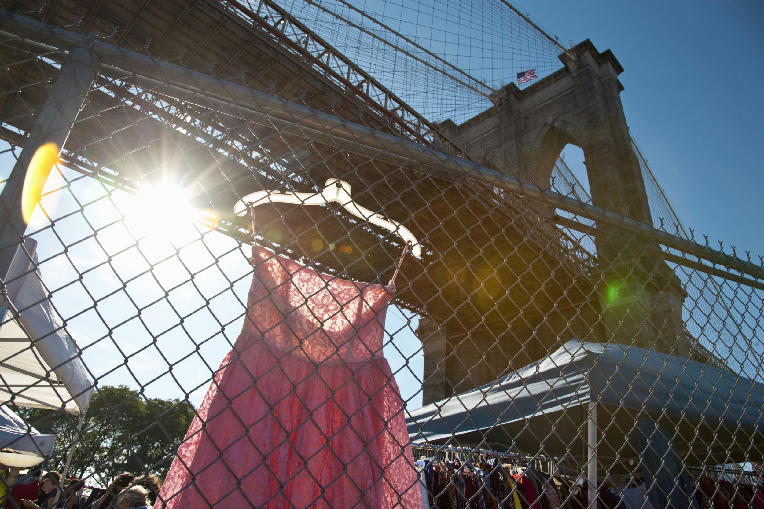 A pink dress hangs on a fence in front of the Brooklyn Bridge in New York City in Winter