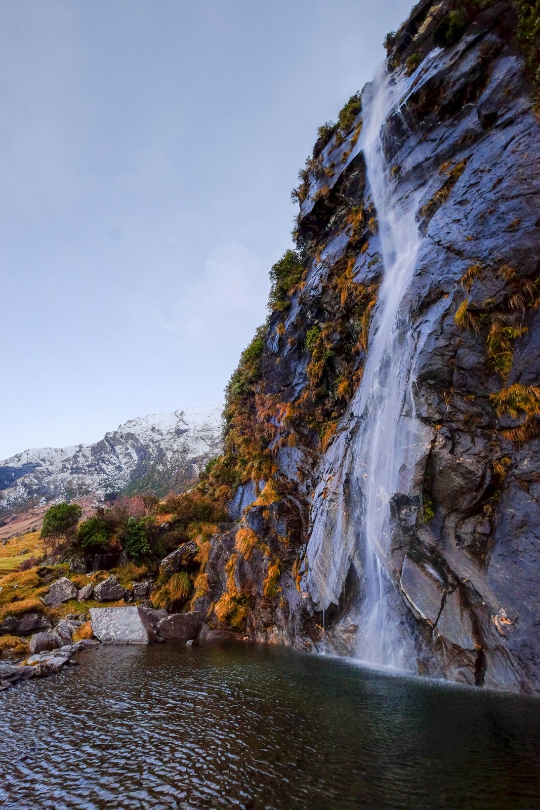 One half of picturesque Wishbone Falls at Mount Aspiring ona sunny day. There are snow-capped mountains in the background.