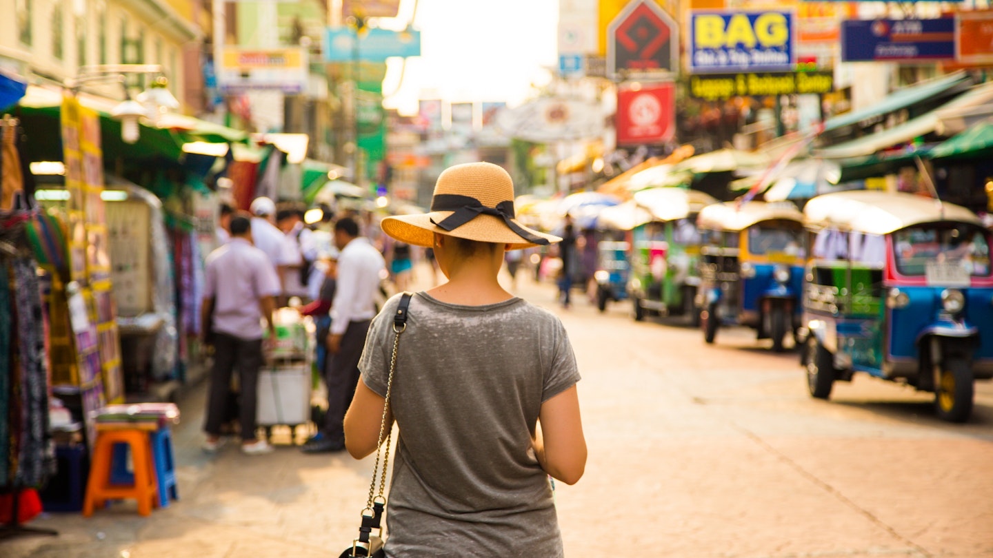 A woman with a hat walking along a shopping street in Bangkok
